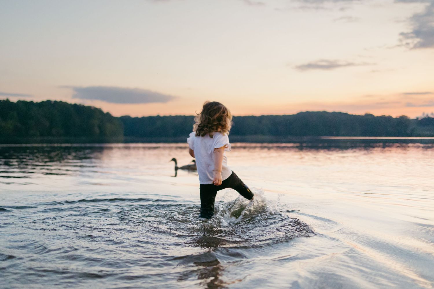 A sequence of silhouettes splashing and playing in a tranquil lake at sunset creates a joyful summer scene.