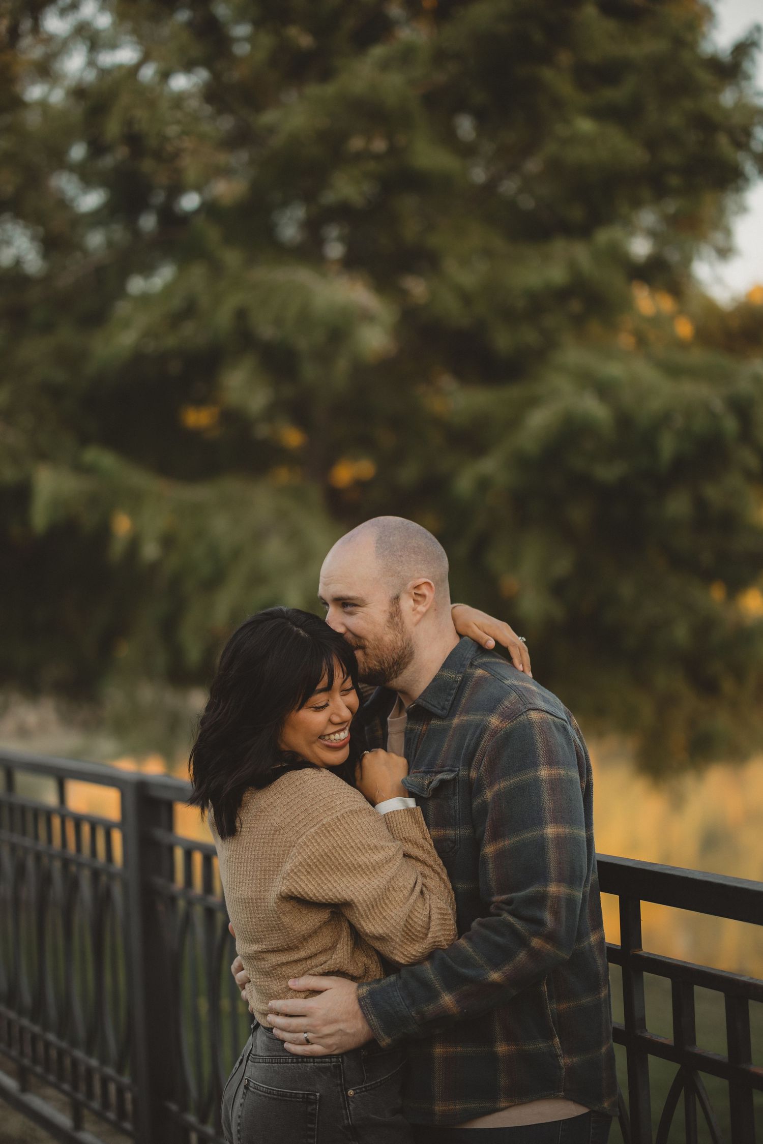 Couple sharing intimate moment while leaning against metal railing at sunset.