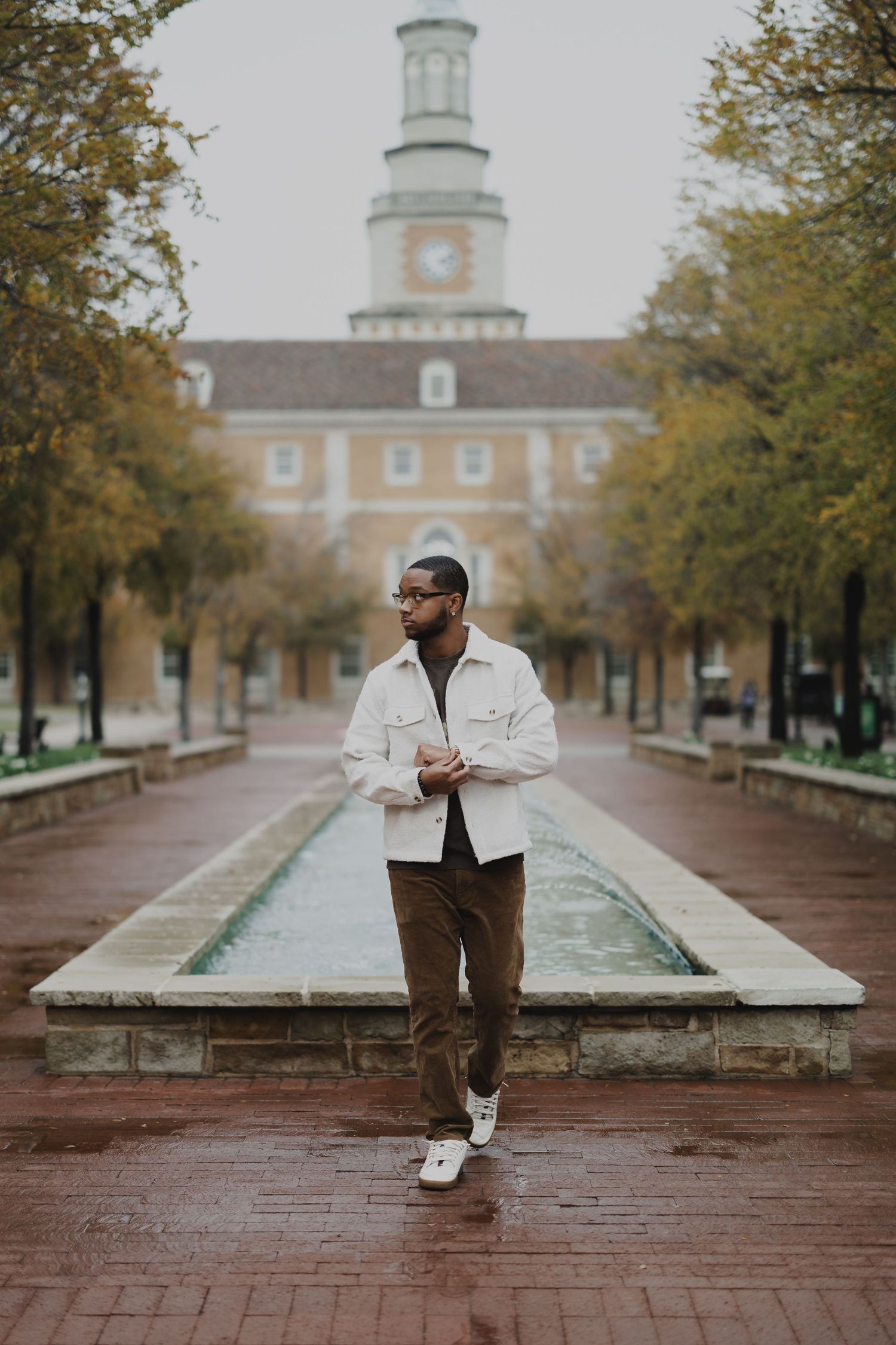 Person in casual attire sits on brick wall in front of historic campus building with clock tower.