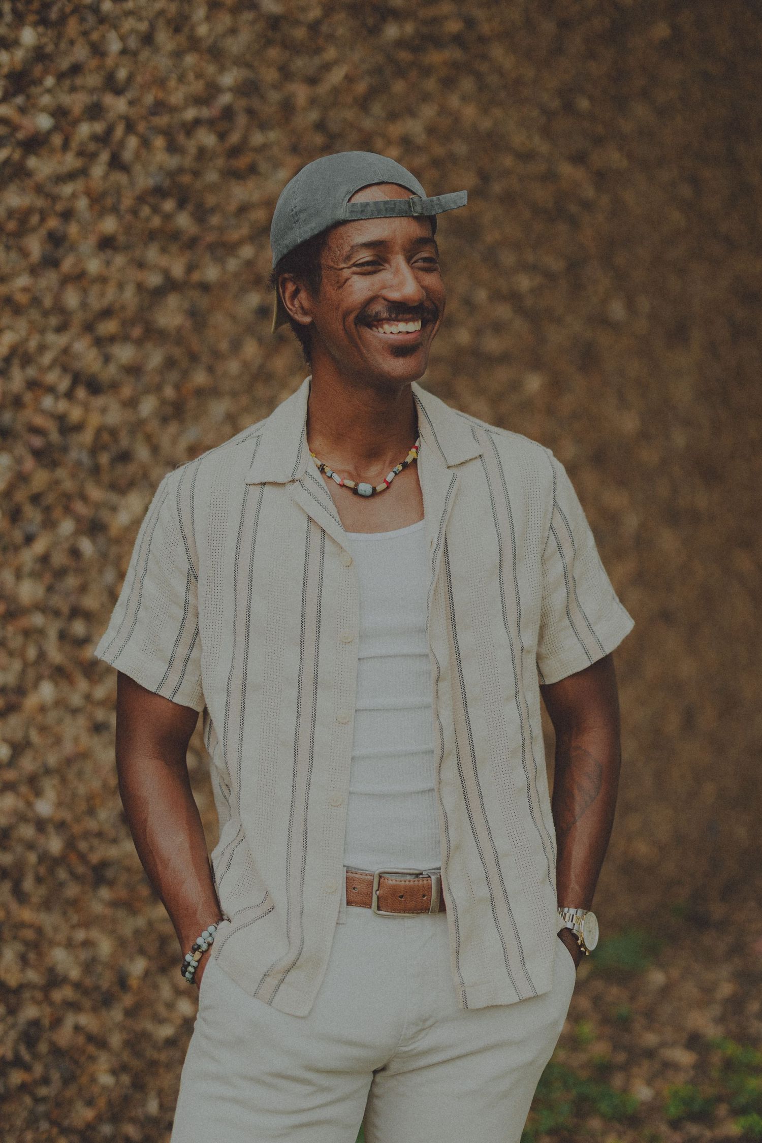 A person wearing light colored clothing and a cap smiles warmly in a series of casual outdoor portrait shots.