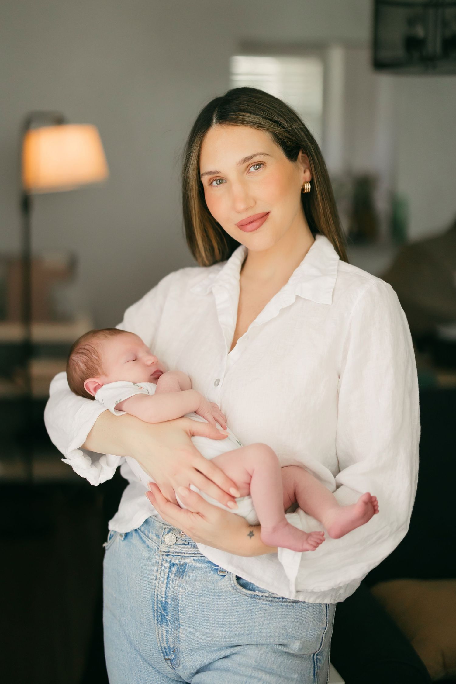 A tender moment captured of someone in a white button-down shirt and jeans holding a sleeping newborn baby.