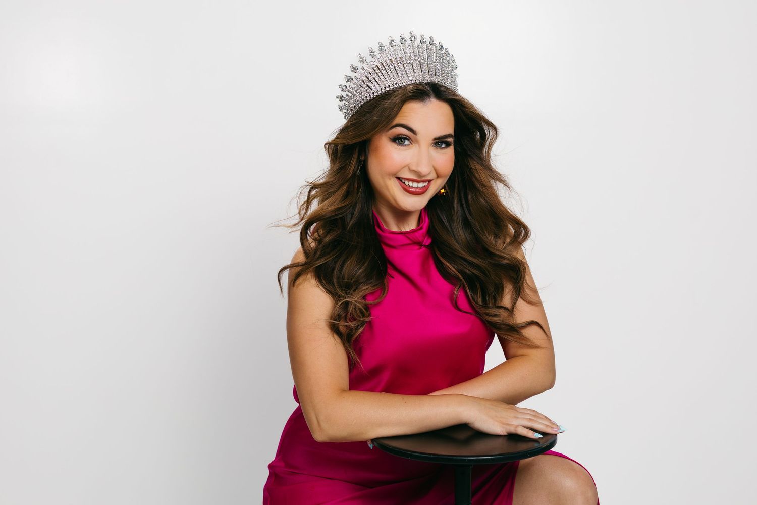 A woman in a vibrant pink dress poses confidently against a light gray studio background.