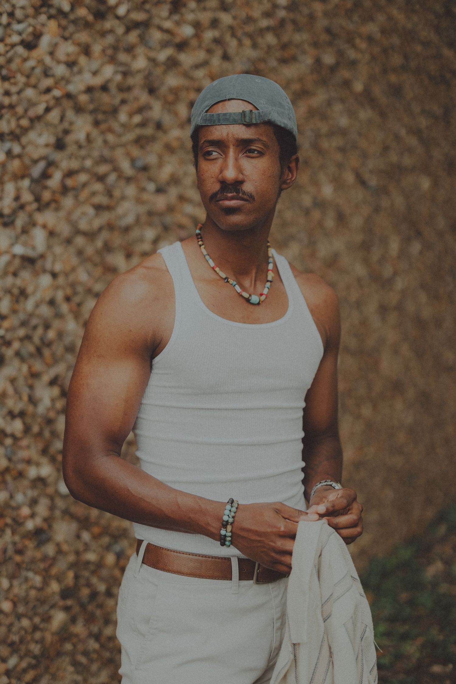 A series of photos showing someone in a white tank top and hat posing against a textured brown background.