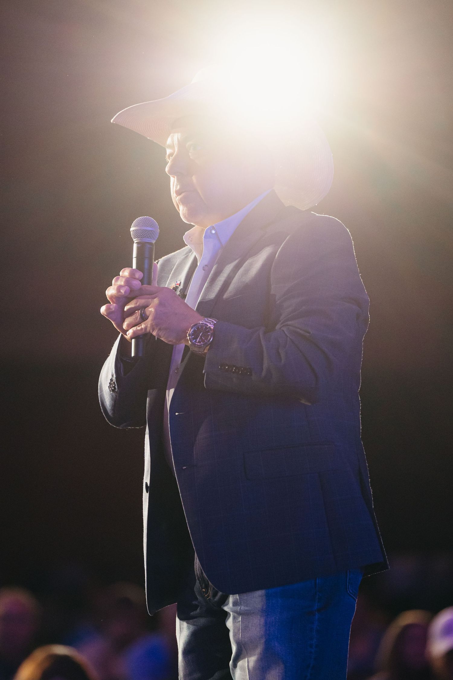 Silhouetted speaker holding microphone against bright stage lighting.