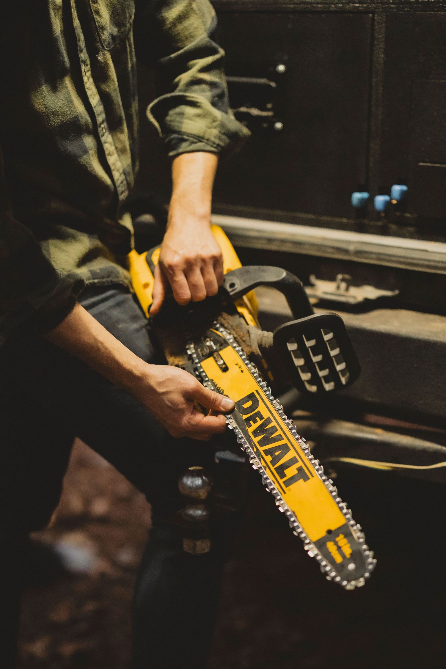 Person holding a yellow DeWalt chainsaw with chain bar visible, wearing green jacket in a dark workshop setting.