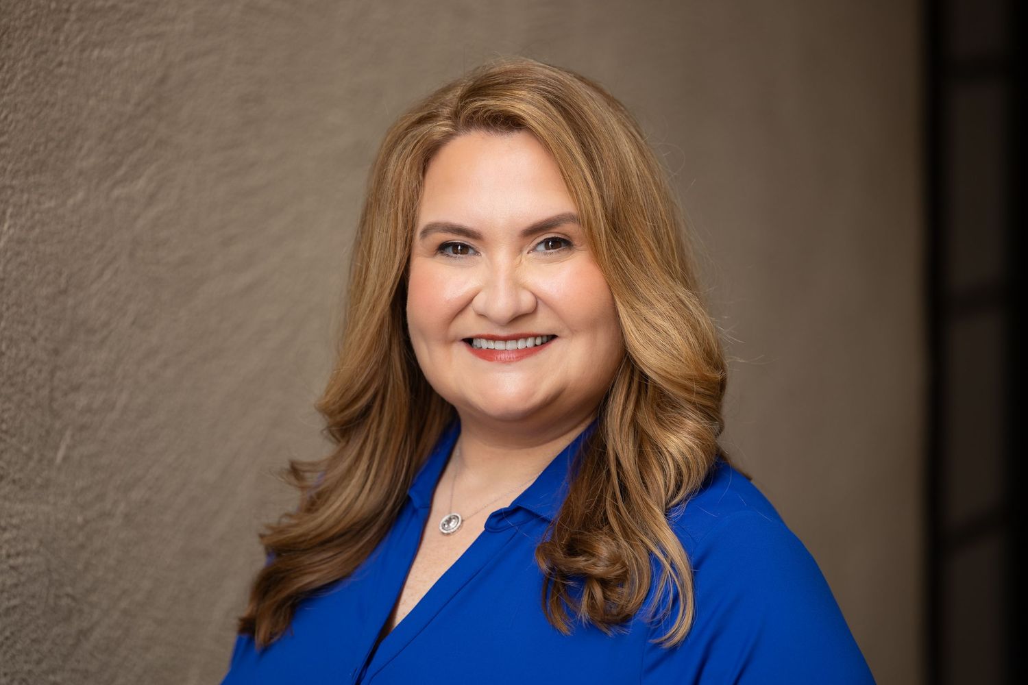 Professional headshot of woman in bright blue blazer against neutral background.