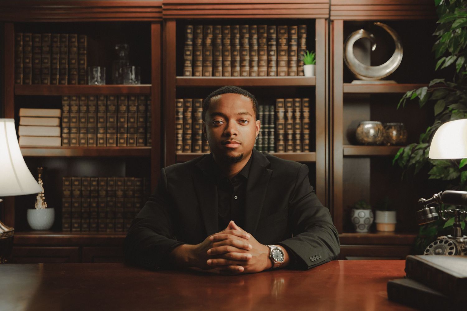 Professional man in suit sits at desk before bookshelf filled with law books in an elegant office setting.