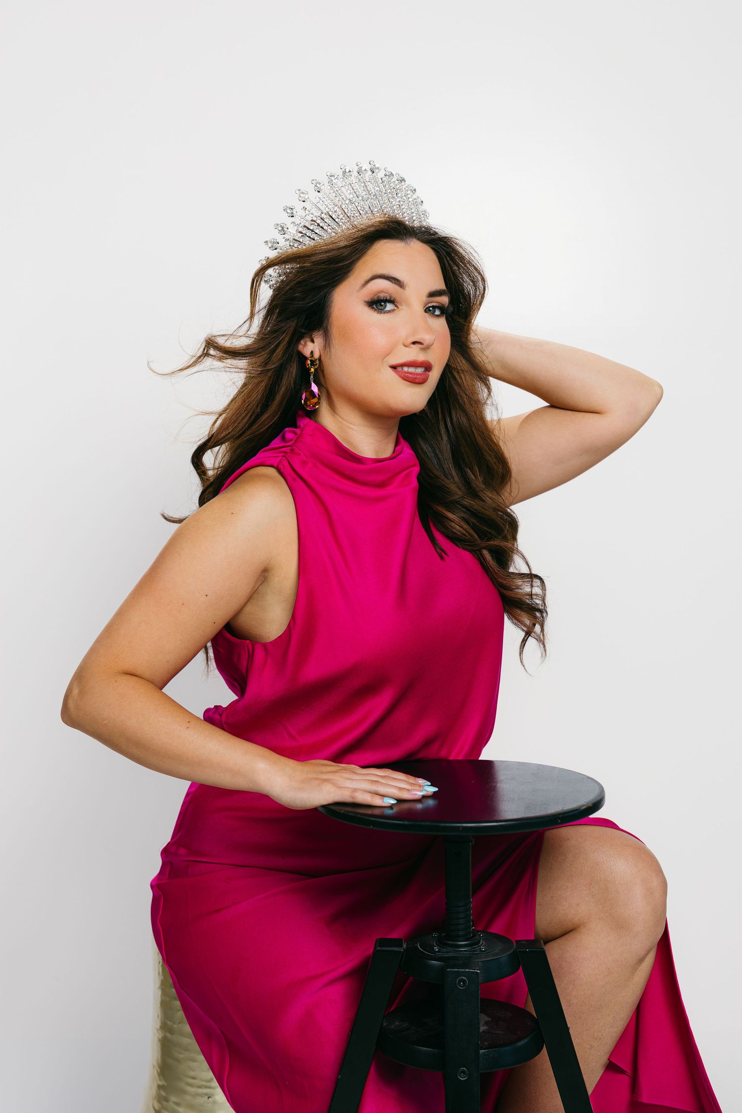 Glamour portrait of woman in magenta dress posing with black chair against white background.