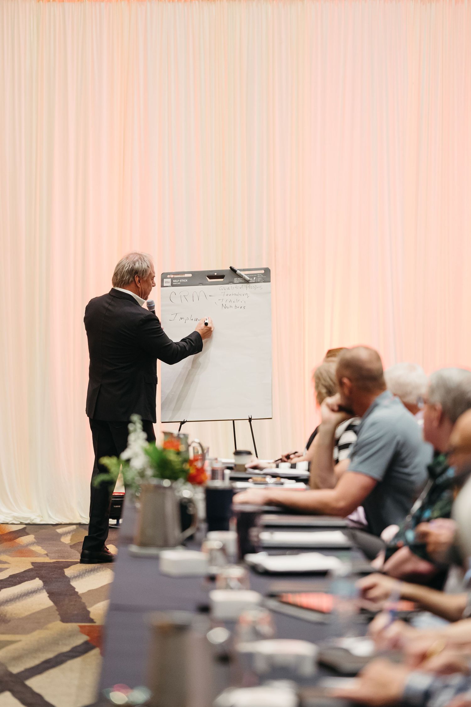 Speaker presents to seated audience in modern conference venue with professional lighting.