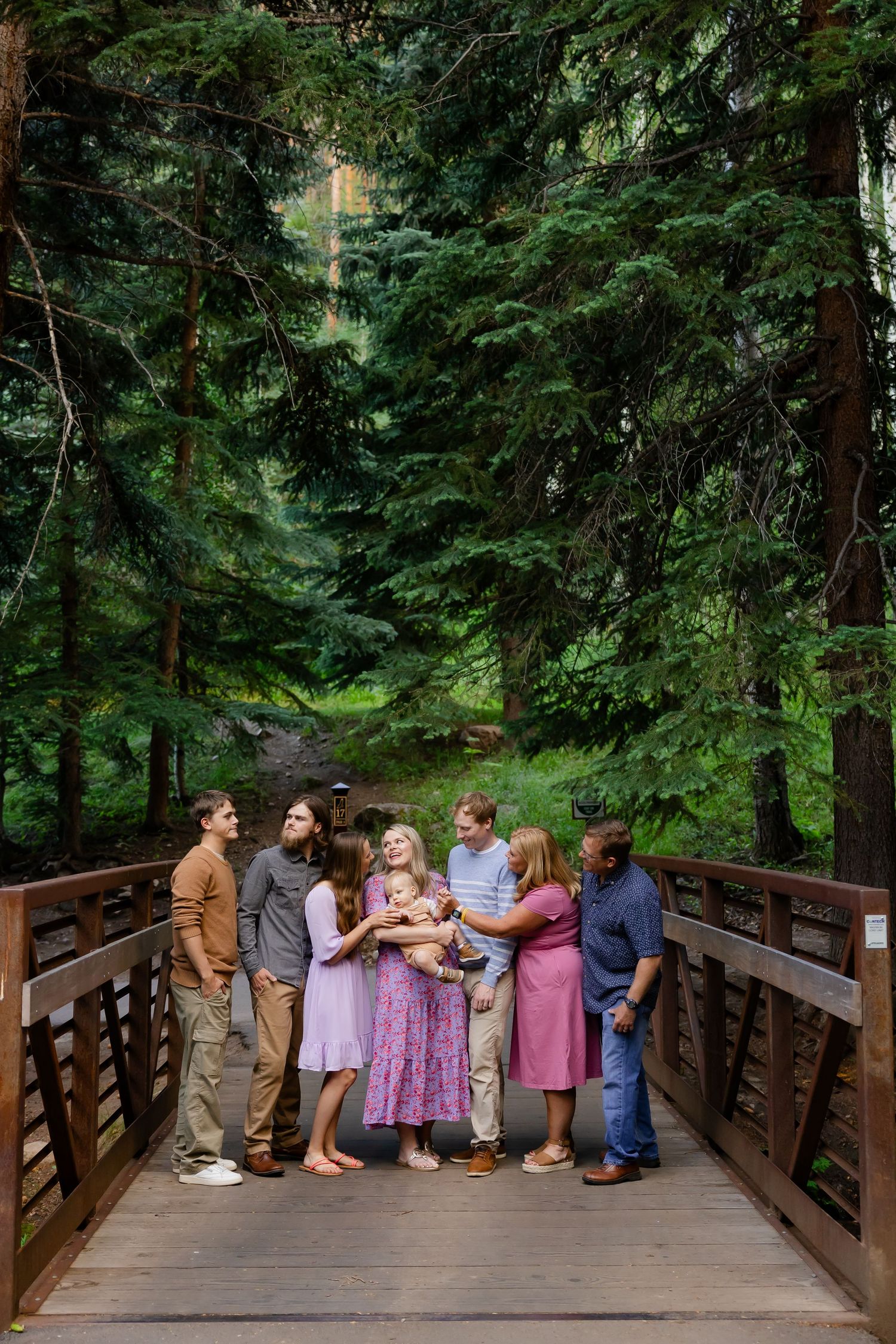 People lined up along a wooden bridge railing in a lush forest setting.