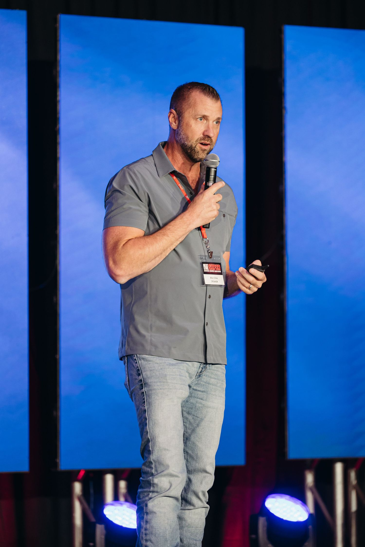 A speaker presents on stage against a blue backdrop during a professional conference or event.