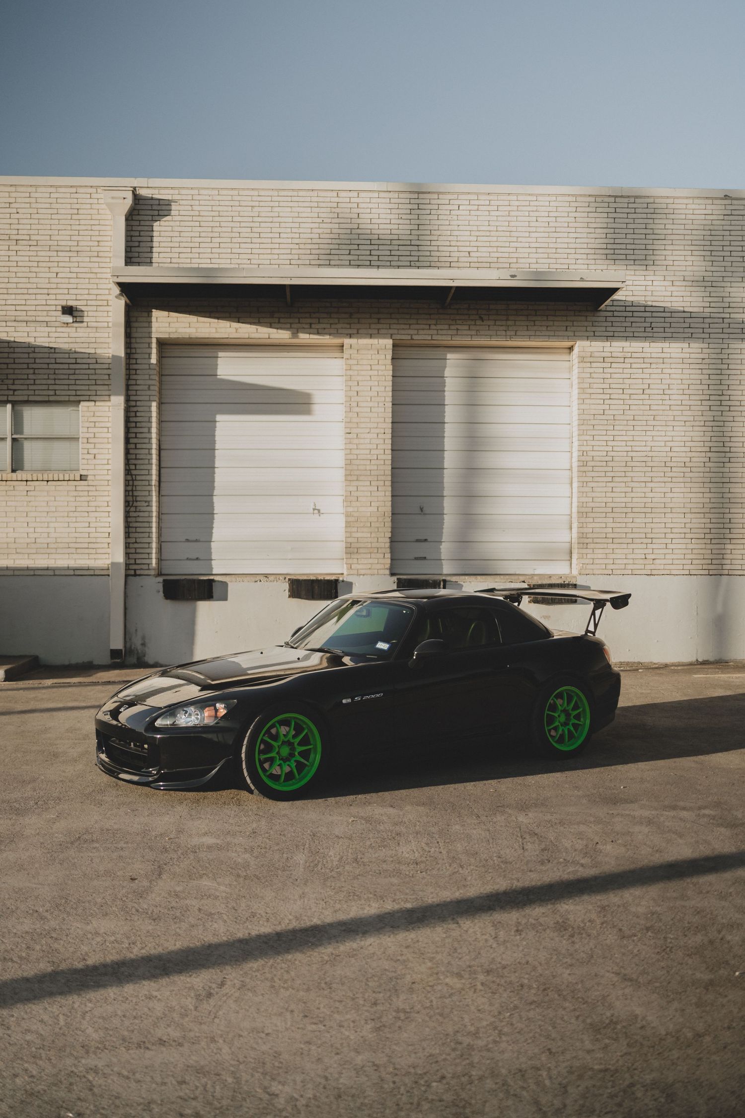 Black sports cars with neon green wheels lined up against brick building exterior.