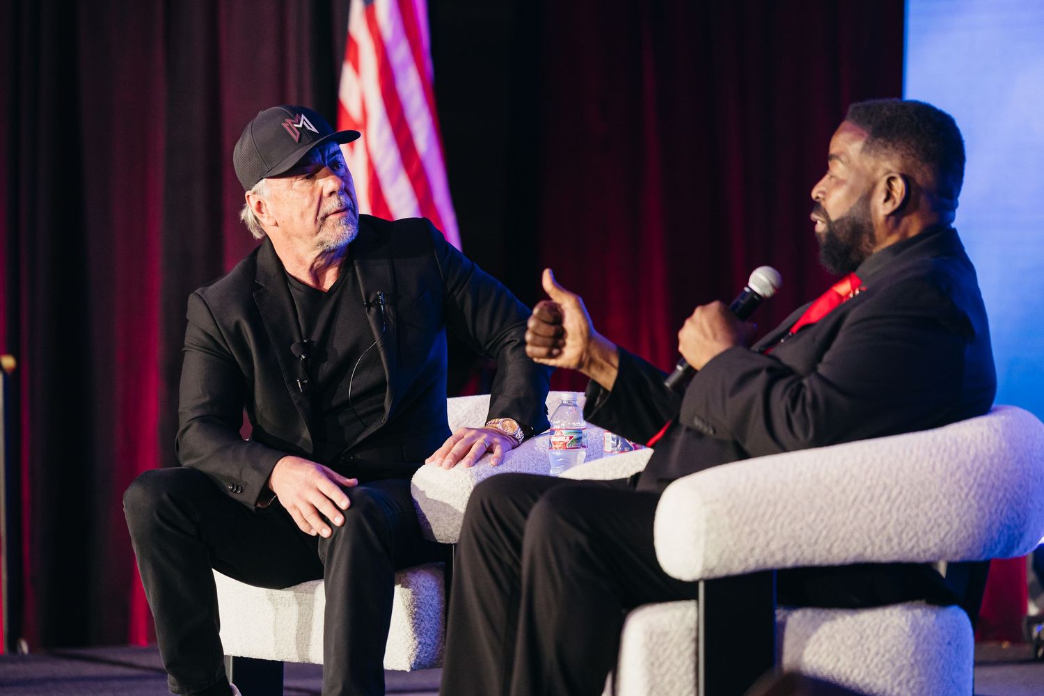 Speaker in casual attire addresses audience at conference panel with microphone.