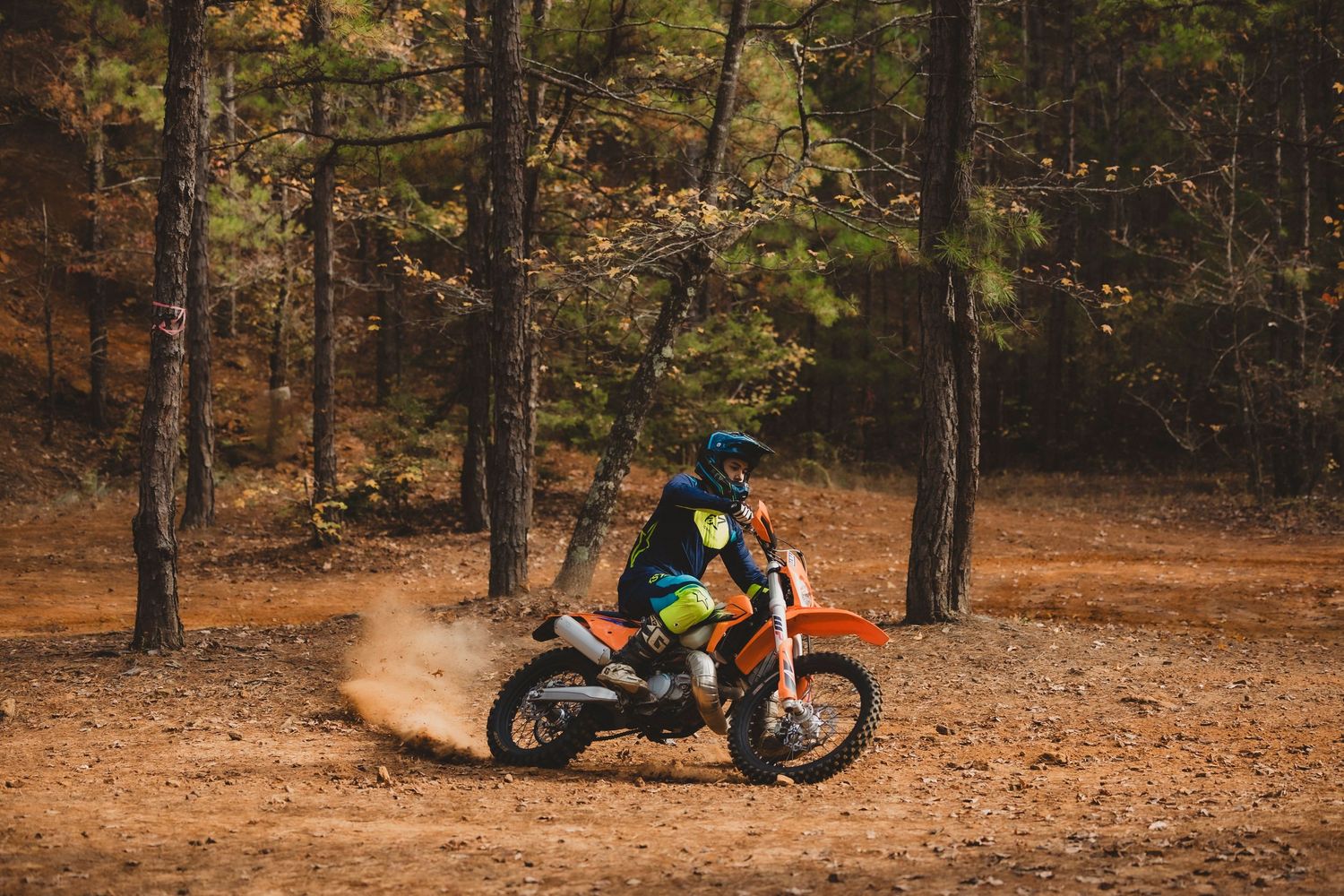 Dirt bike rider kicking up dust while riding through a wooded trail.