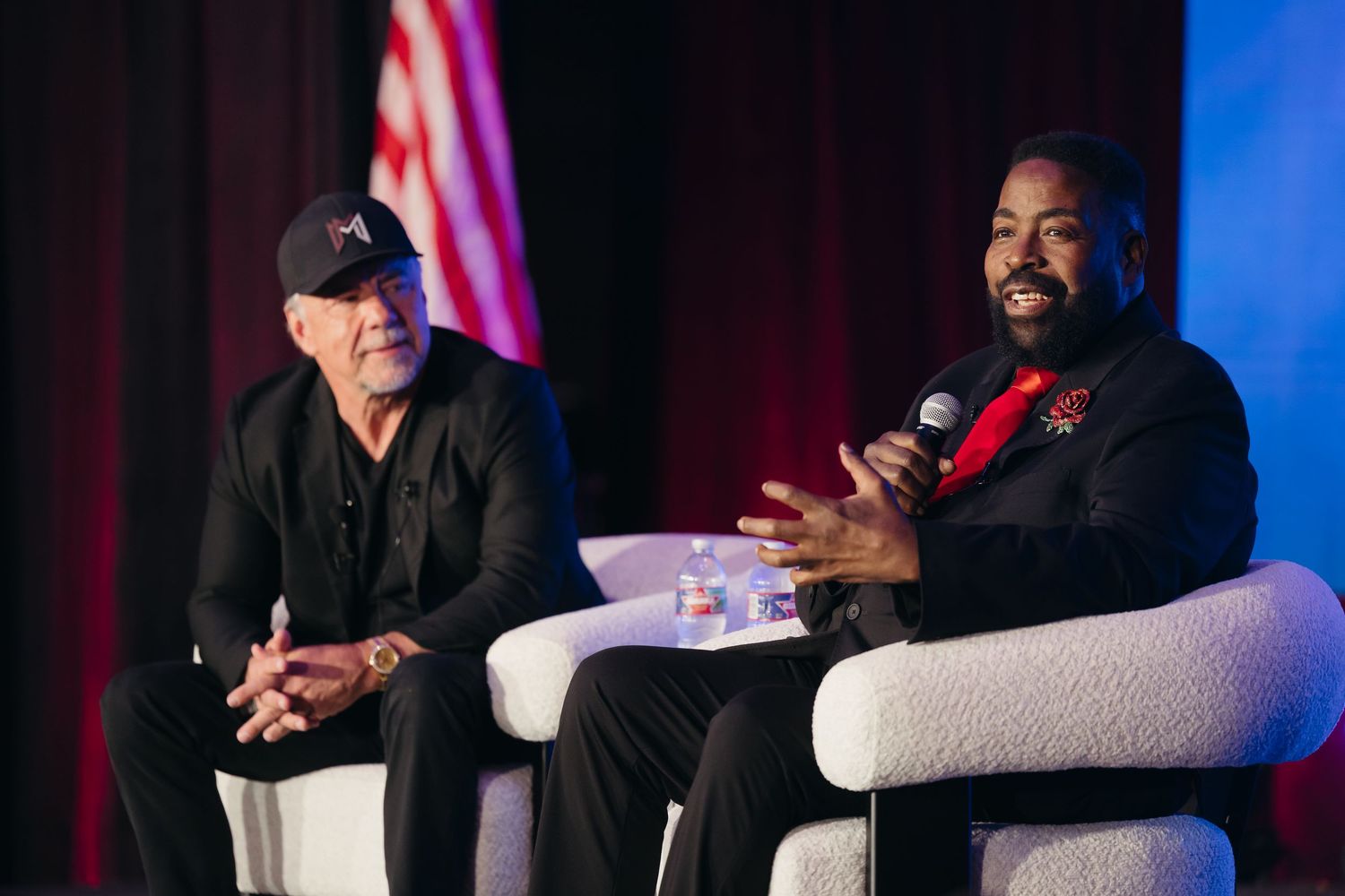 Panel discussion setup with speakers seated in chairs on stage with red and blue lighting.