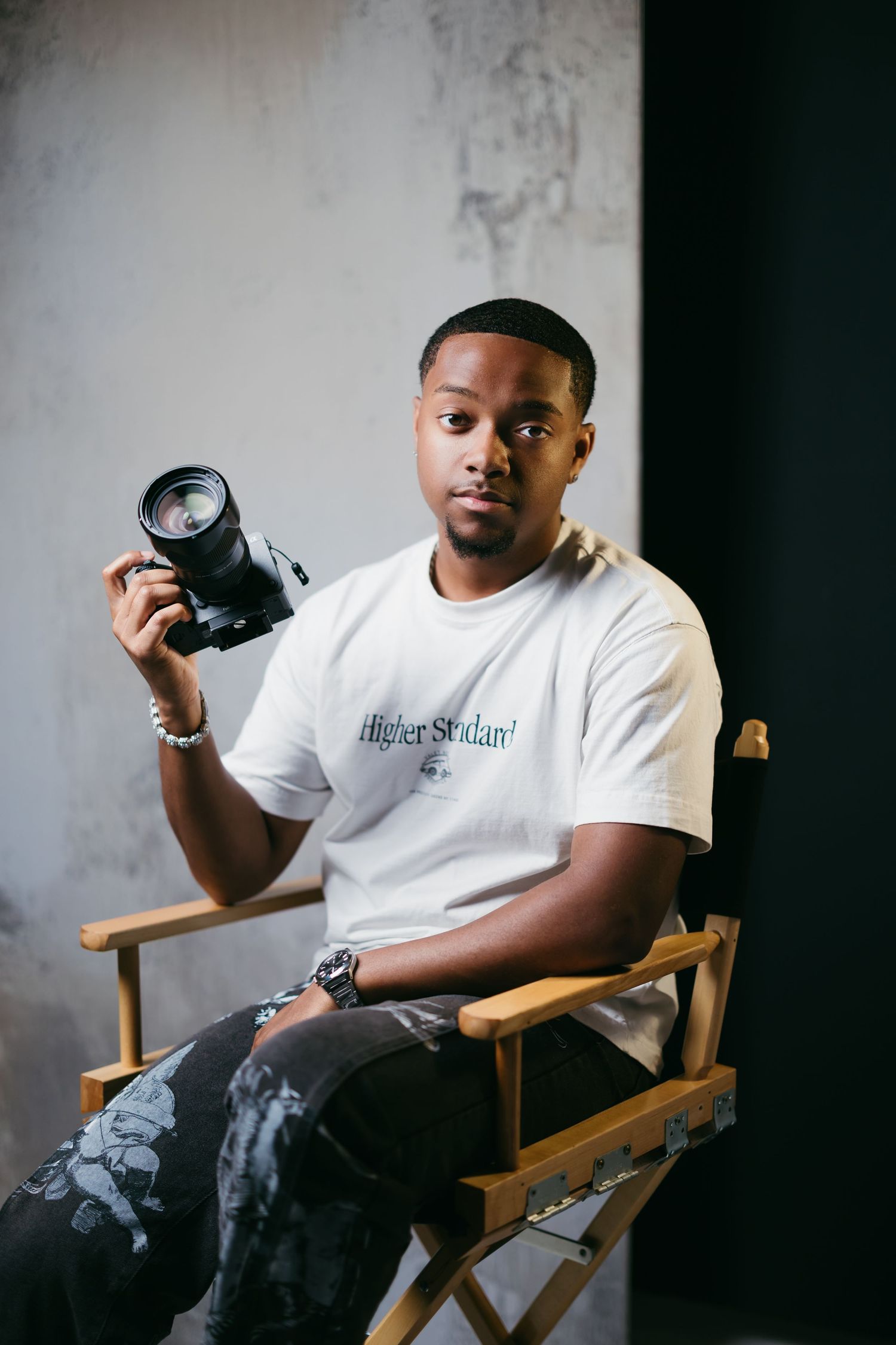 Photographer in white t-shirt holding camera while seated in director's chair.
