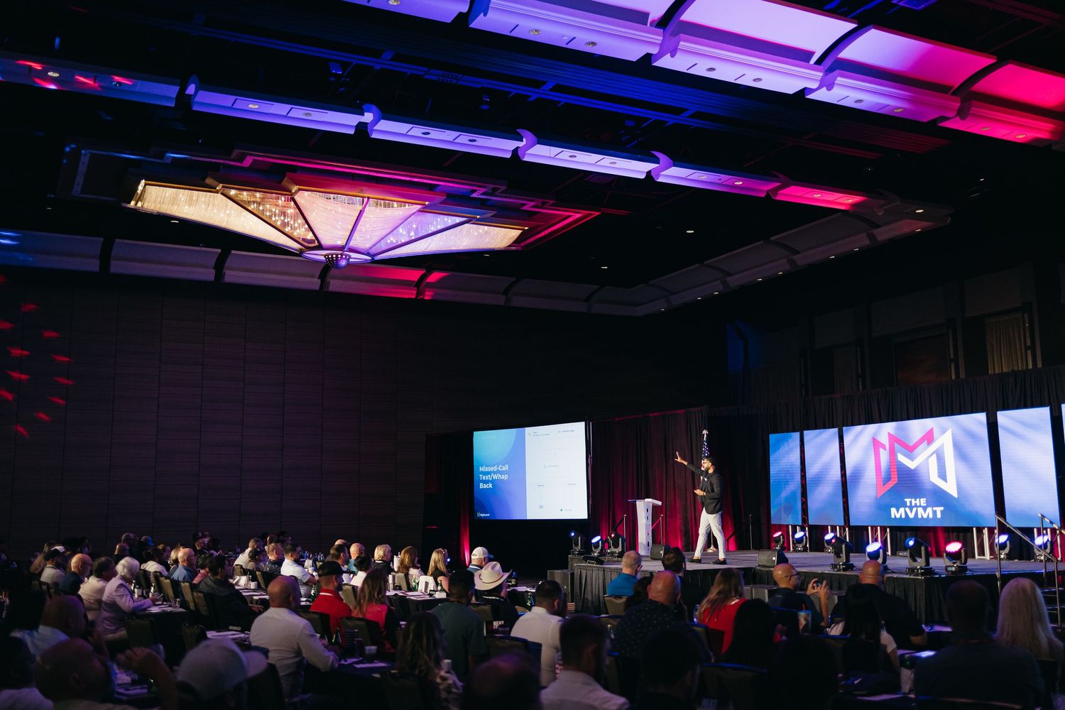 Large conference room with dramatic pink and blue lighting showing audience seating and stage setup.