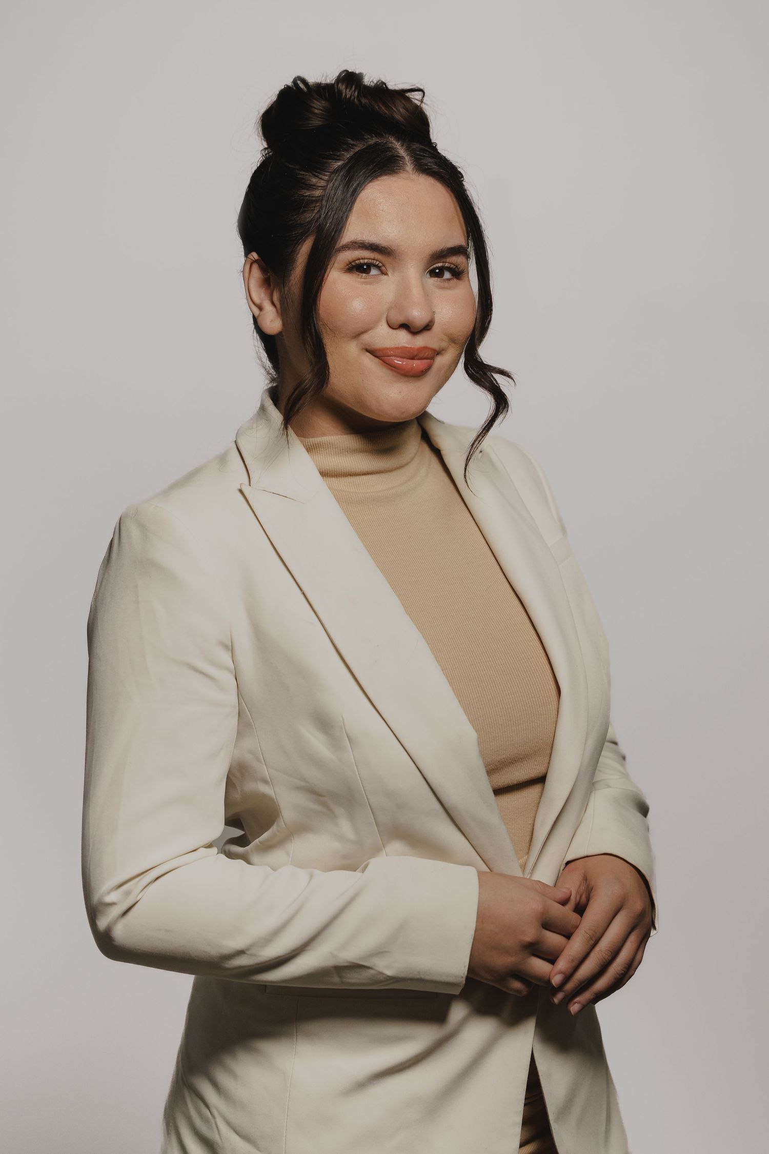 Portrait session featuring person in cream blazer and tan top against light background.