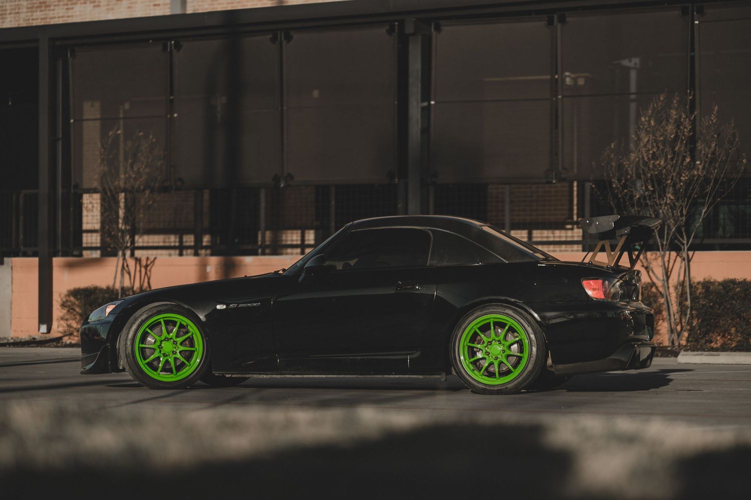 Black sports car with bright green wheels parked on a street at dusk.