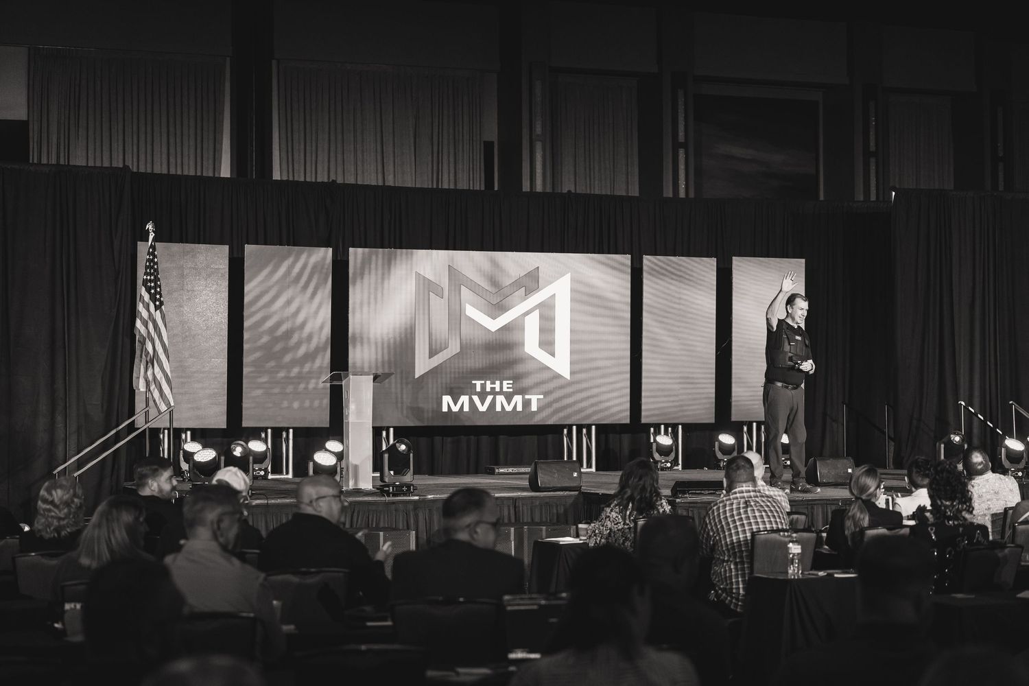 Conference stage with modern multimedia display showing MVMT logo in black and white.