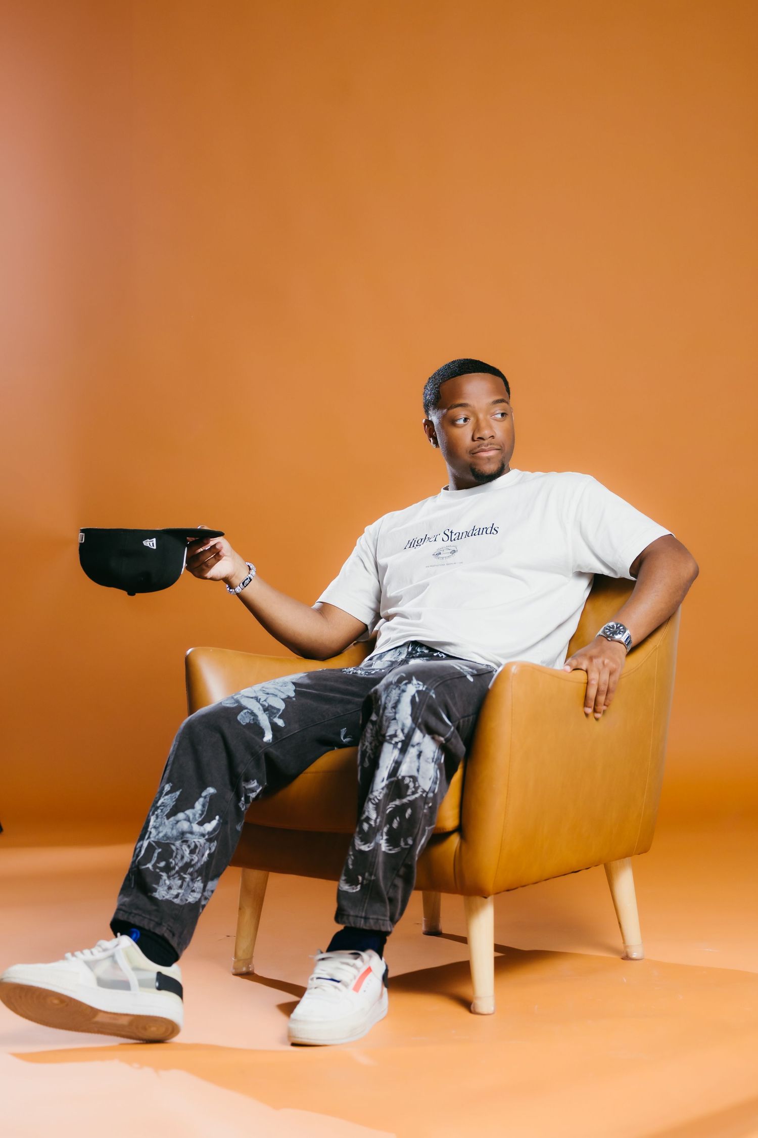 Person lounging casually on yellow chair against orange backdrop in multiple poses.