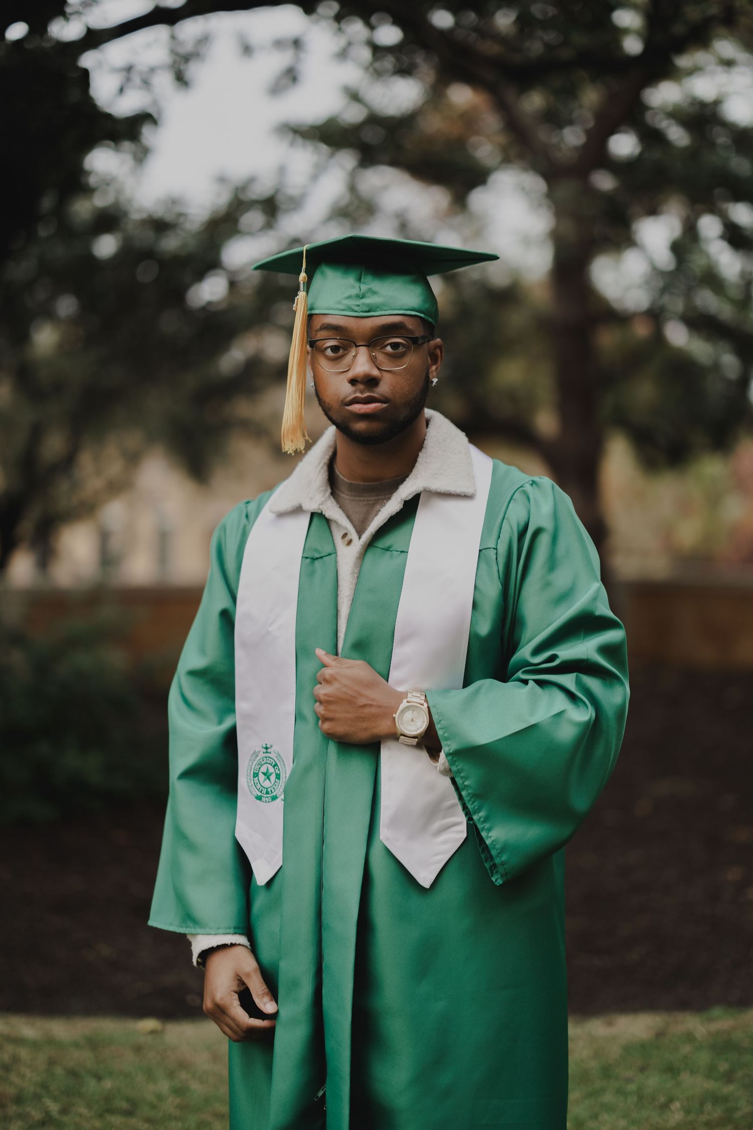 Graduate wearing green academic regalia and stole poses for portrait outdoors.