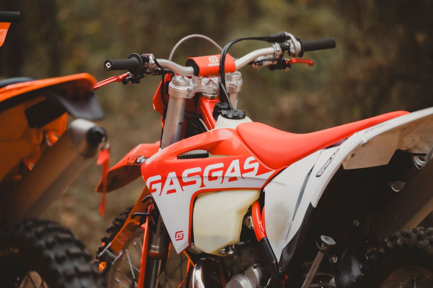 Orange GASGAS dirt bike parked outdoors on a trail, showcasing its bold branding and motocross design.