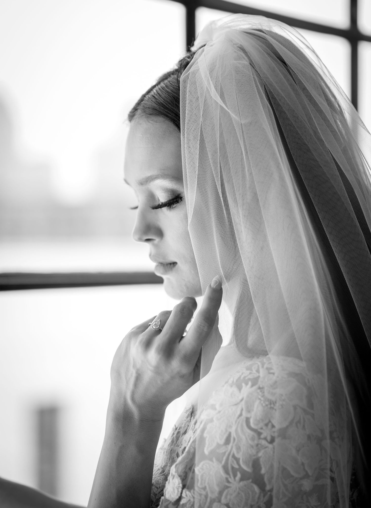 A black and white photo series showing a bride in a delicate veil looking down in contemplative poses by a window.
