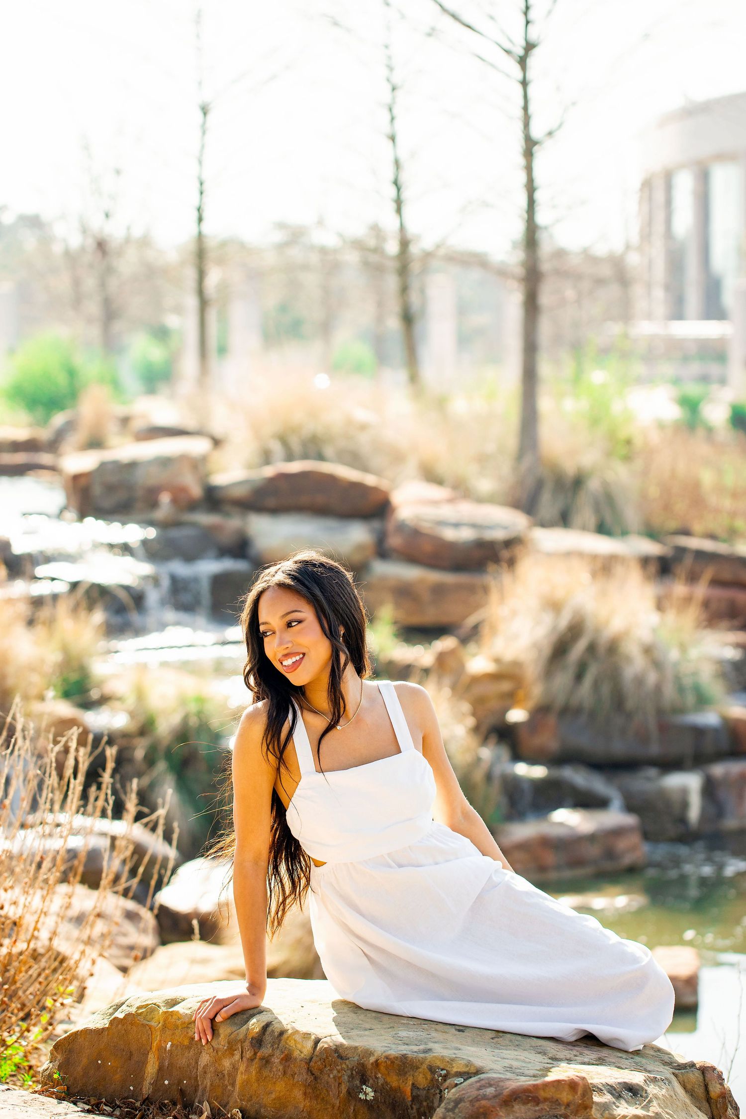 Outdoor photoshoot on decorative rocks near a water feature with natural lighting.
