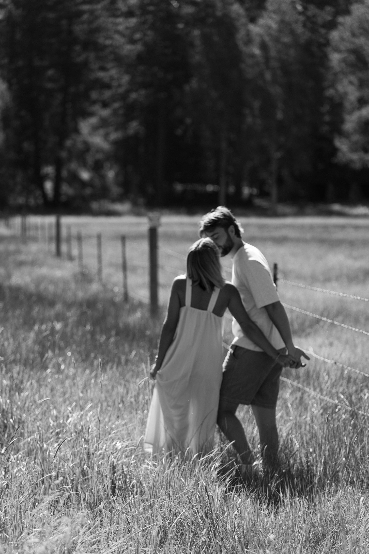 Black and white photo of a couple sharing a romantic moment in a grassy field with trees in the background.