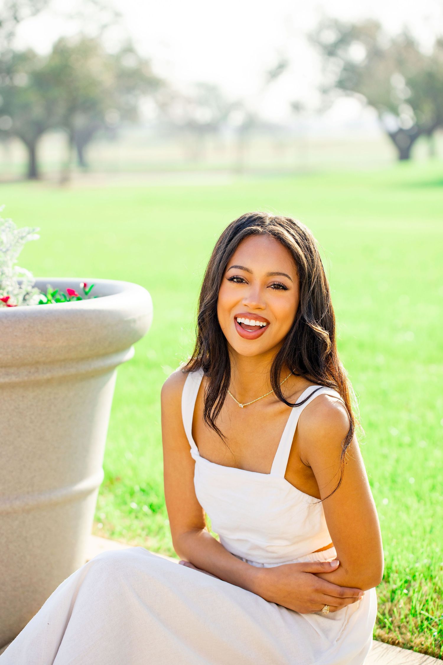 Joyful graduation portraits taken on grassy lawn with white planter in background.