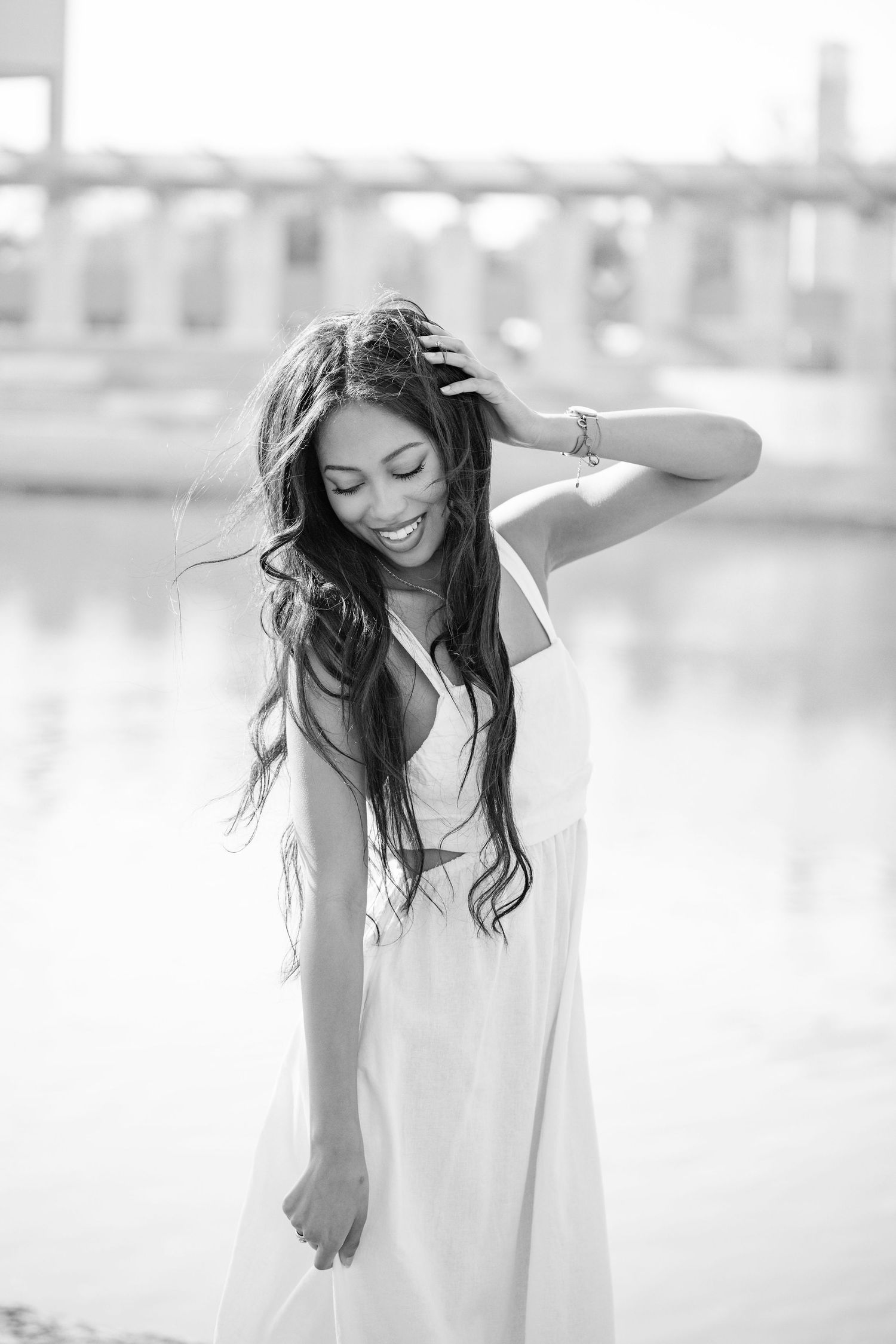A person in a white dress laughs joyfully while twirling with flowing dark hair against a bright, soft-focus background.
