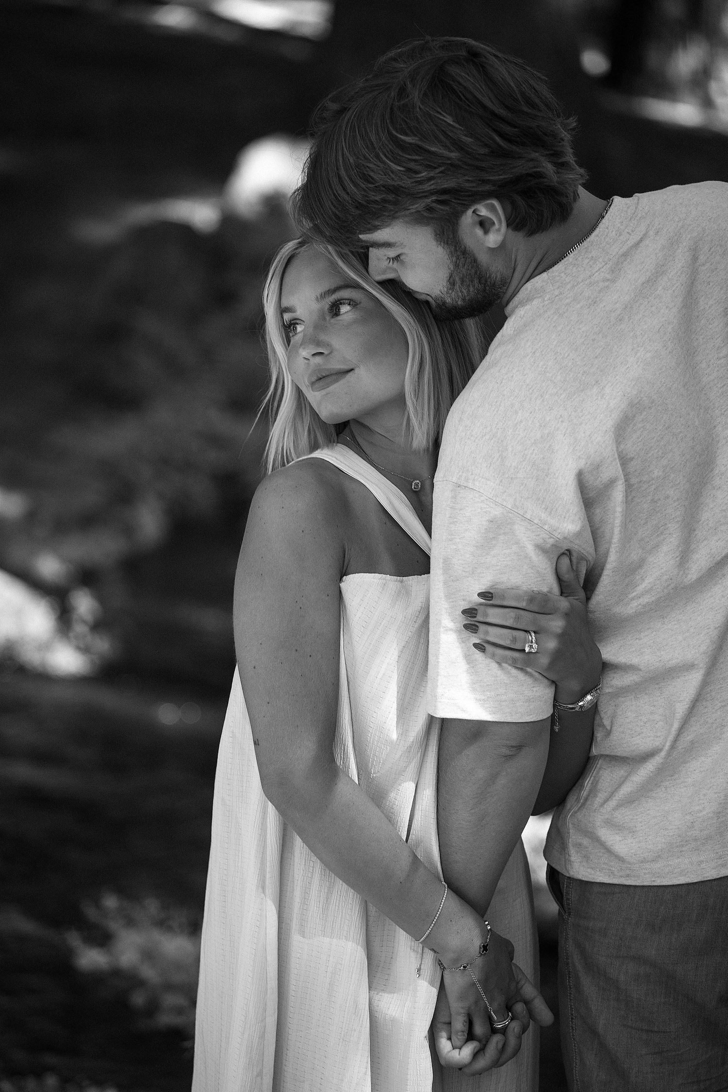 Black and white photo of a couple holding hands, woman in white dress gazing up as man leans in close.
