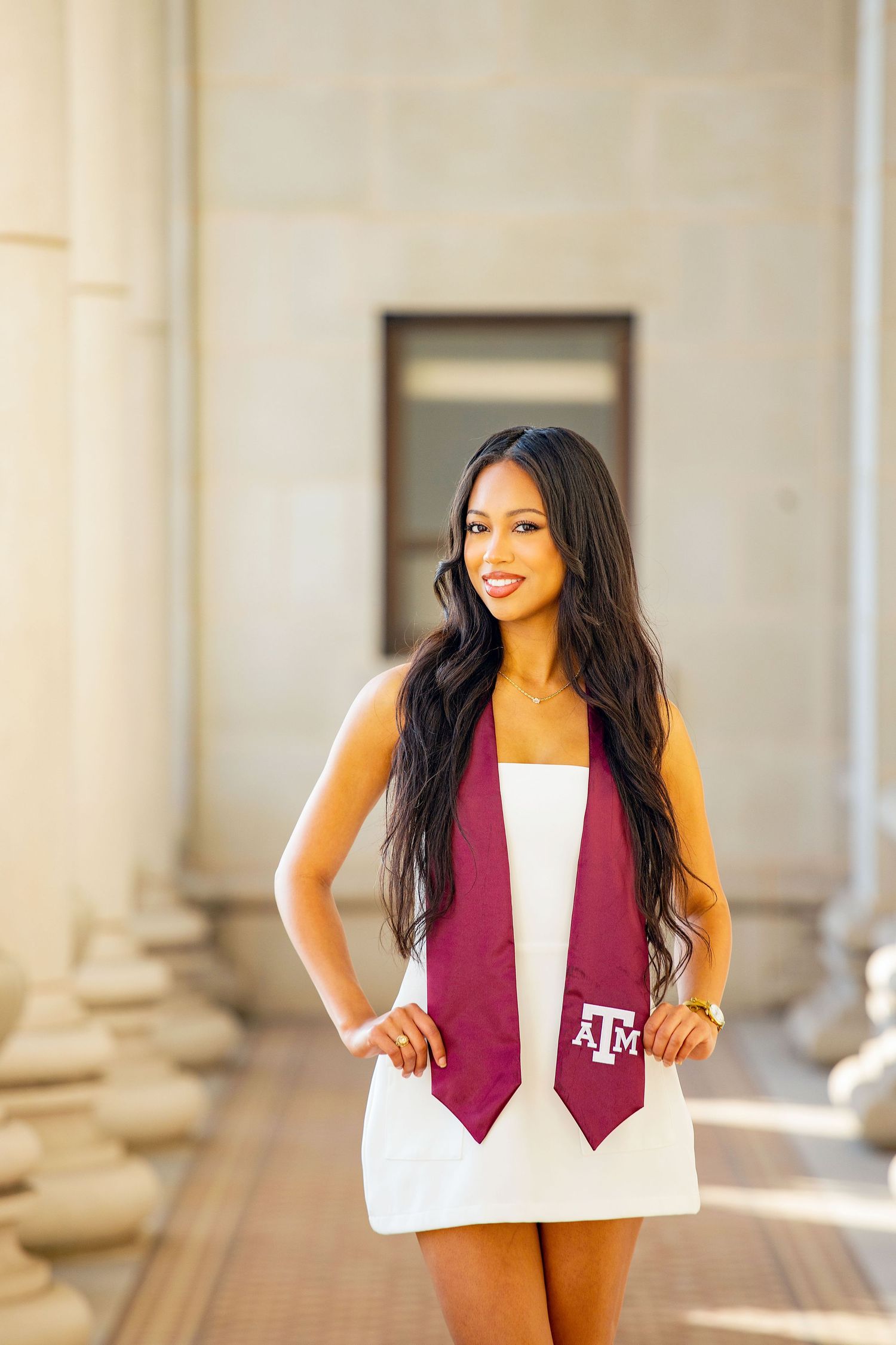 Graduate wearing Texas A&M stole poses between white columns during outdoor photo session.