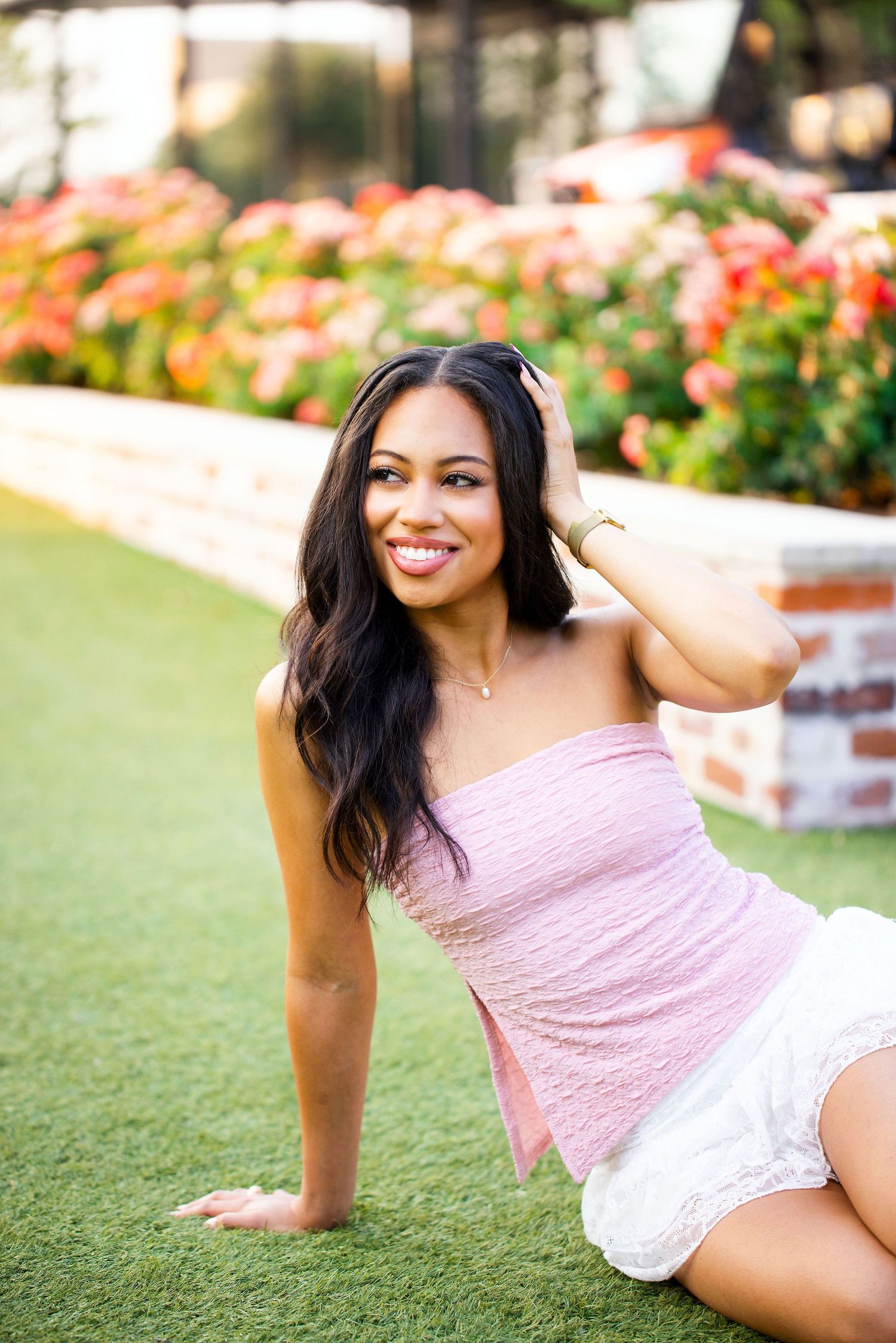 Texas A&M University graduate in pink top and white skirt photographed in Century Square in a garden setting with blooming roses.