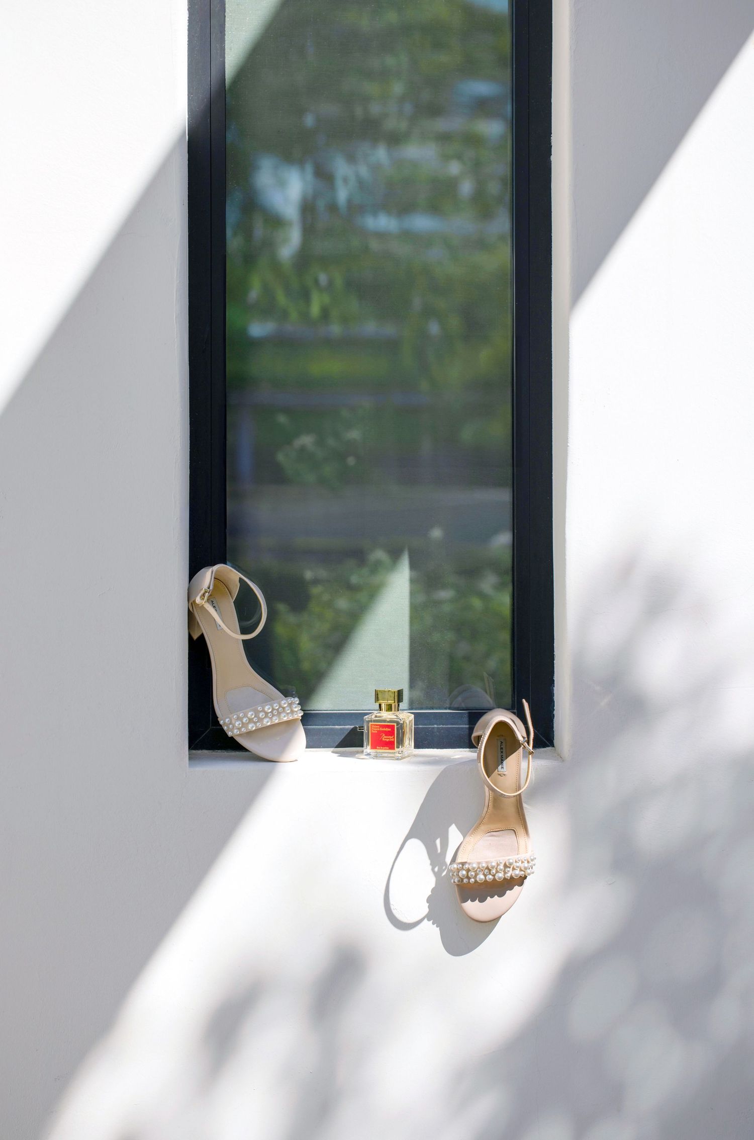 Elegant bridal shoes and a perfume bottle are displayed on a windowsill with dramatic shadows in Scottsdale, Arizona.