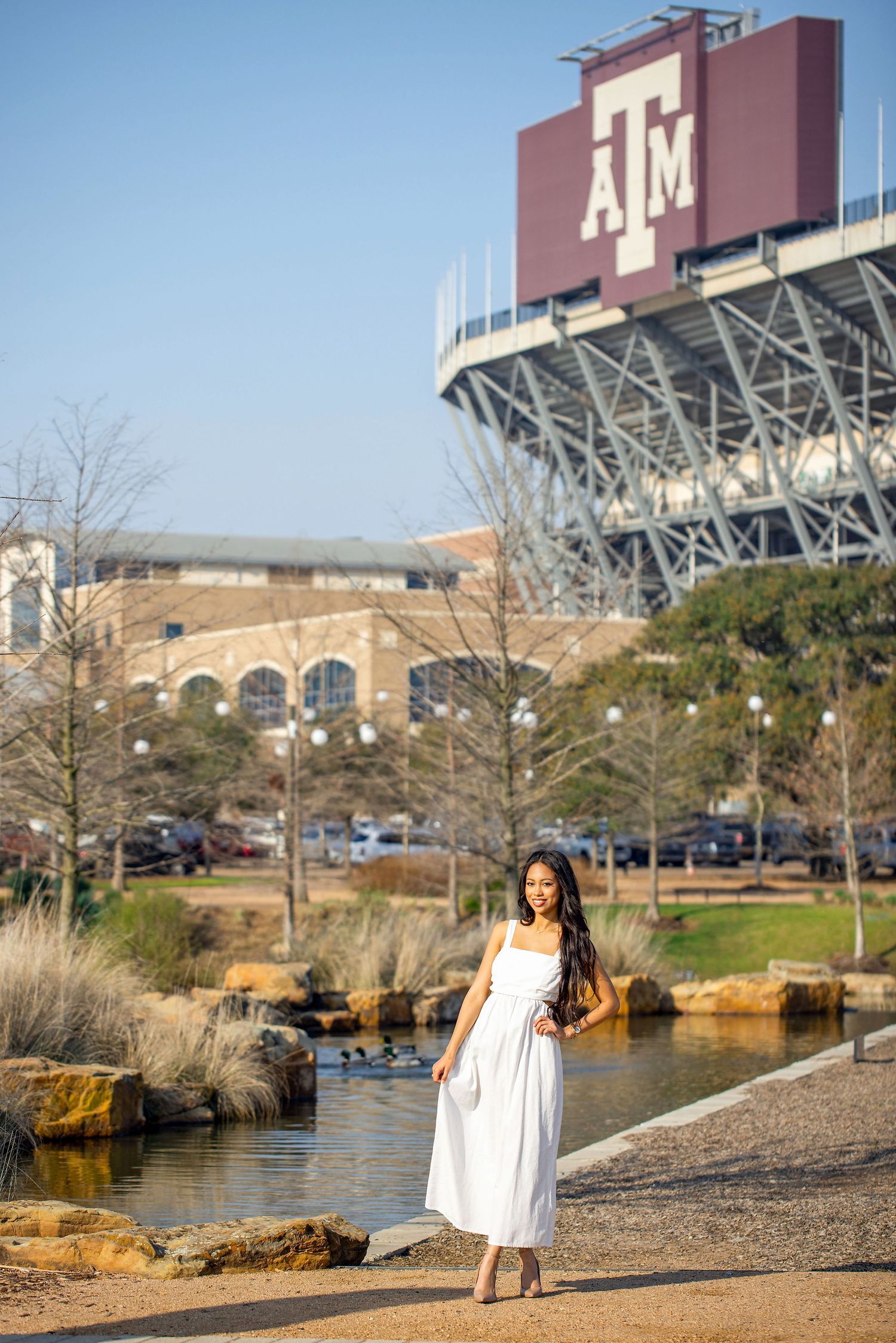 White dress photoshoot near Texas A&M stadium with water features in the background.