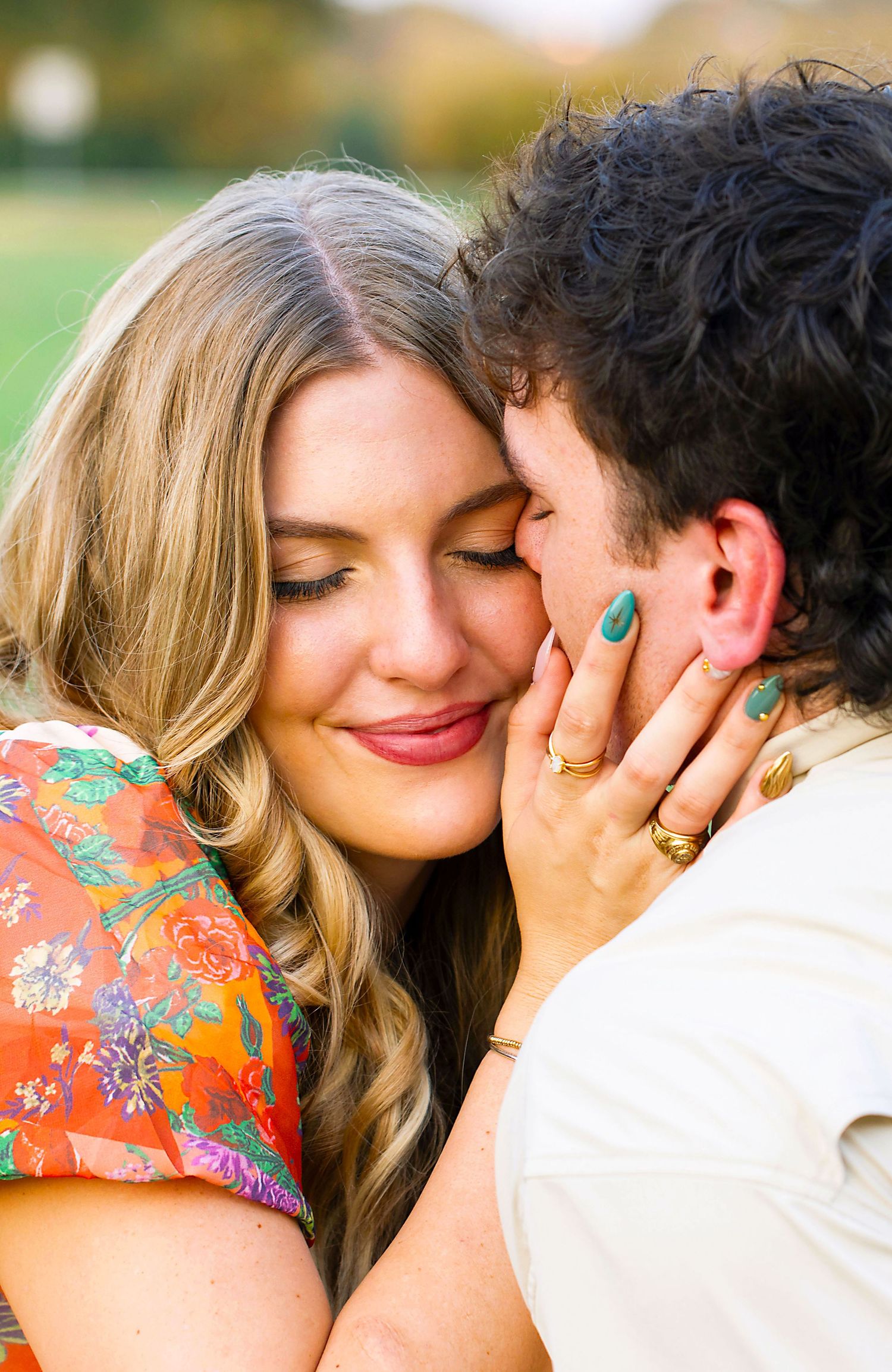 A tender romantic moment between a couple, with her wearing a floral orange top and teal nail polish.