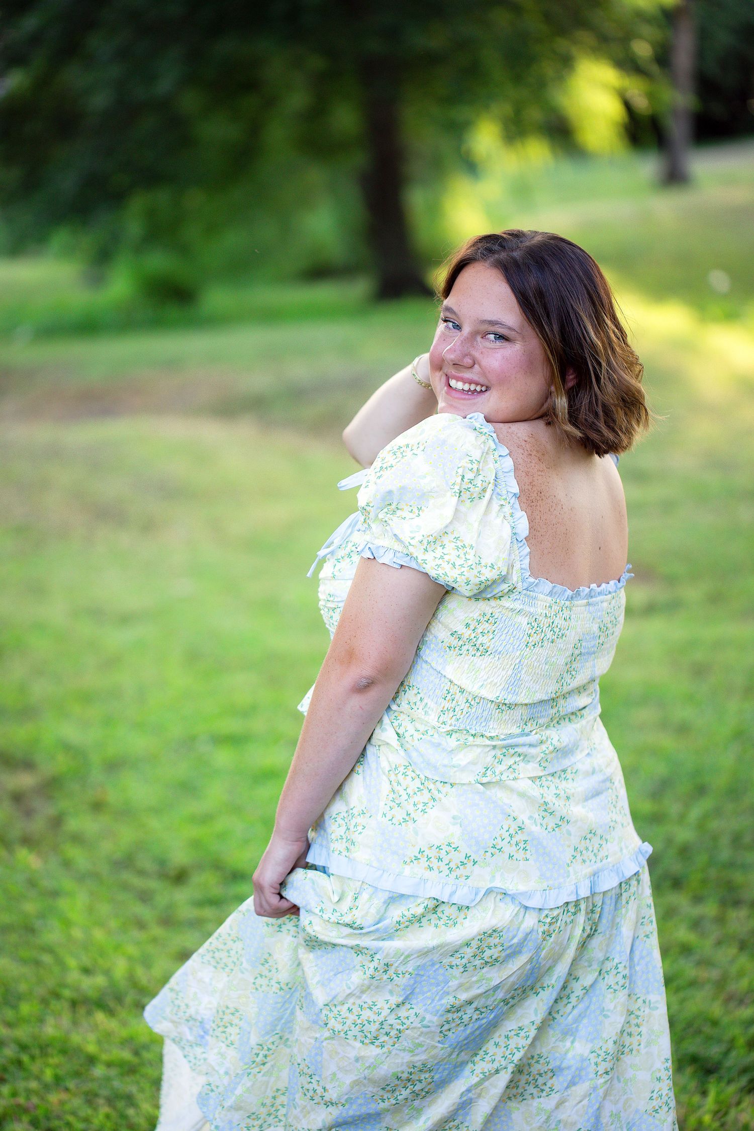 Woman in floral summer dress twirls joyfully in a sunlit garden setting.