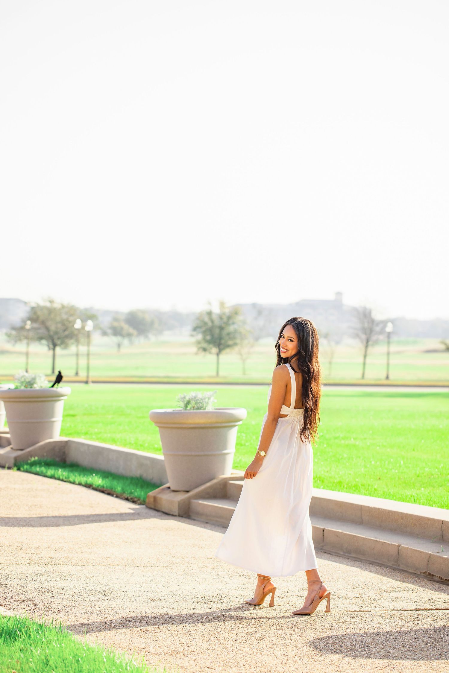 White dress stands out against lush green grass and stone architecture in outdoor photoshoot.
