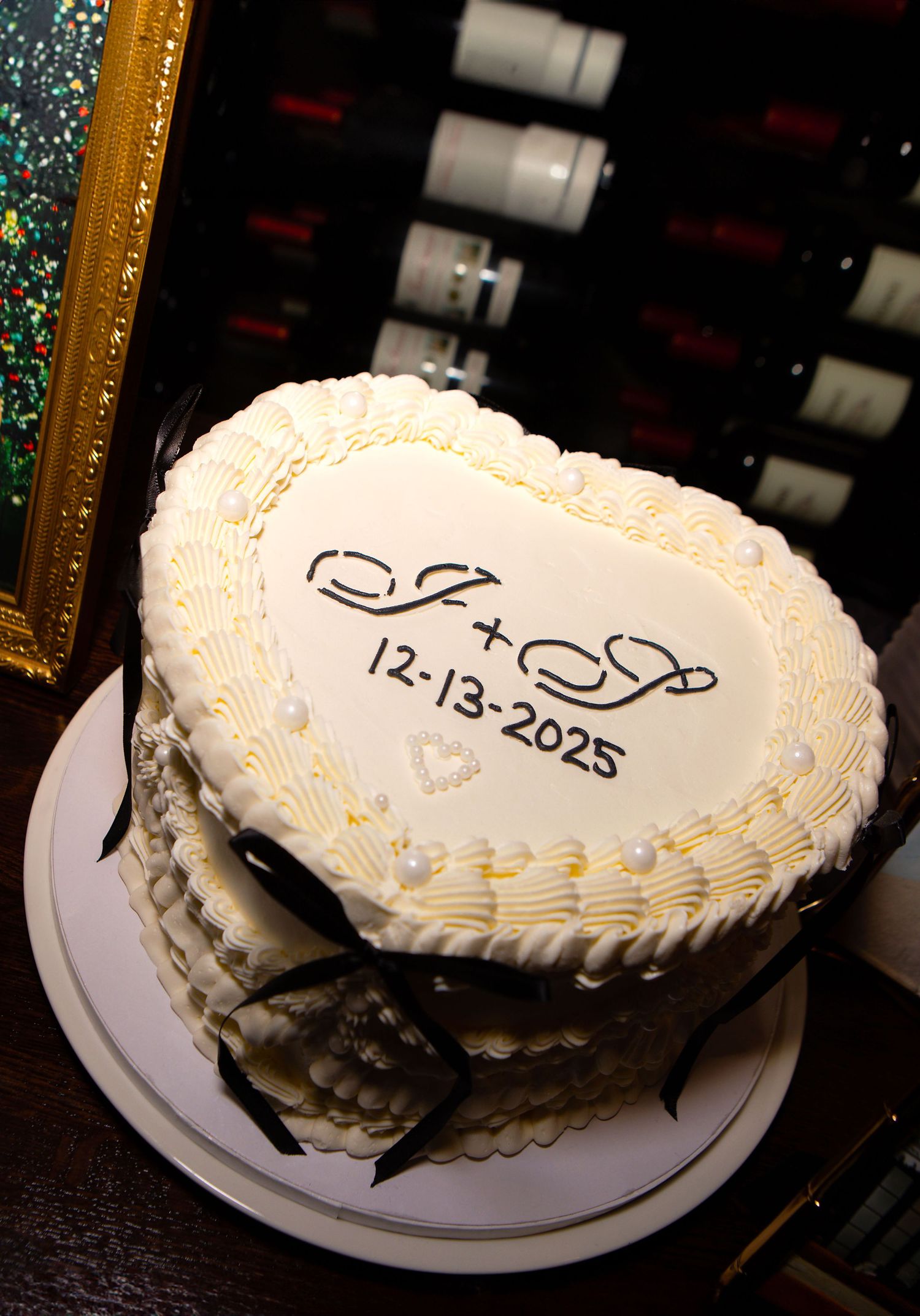 A white wedding cake with decorative piping and a date inscription displayed against a dark background.