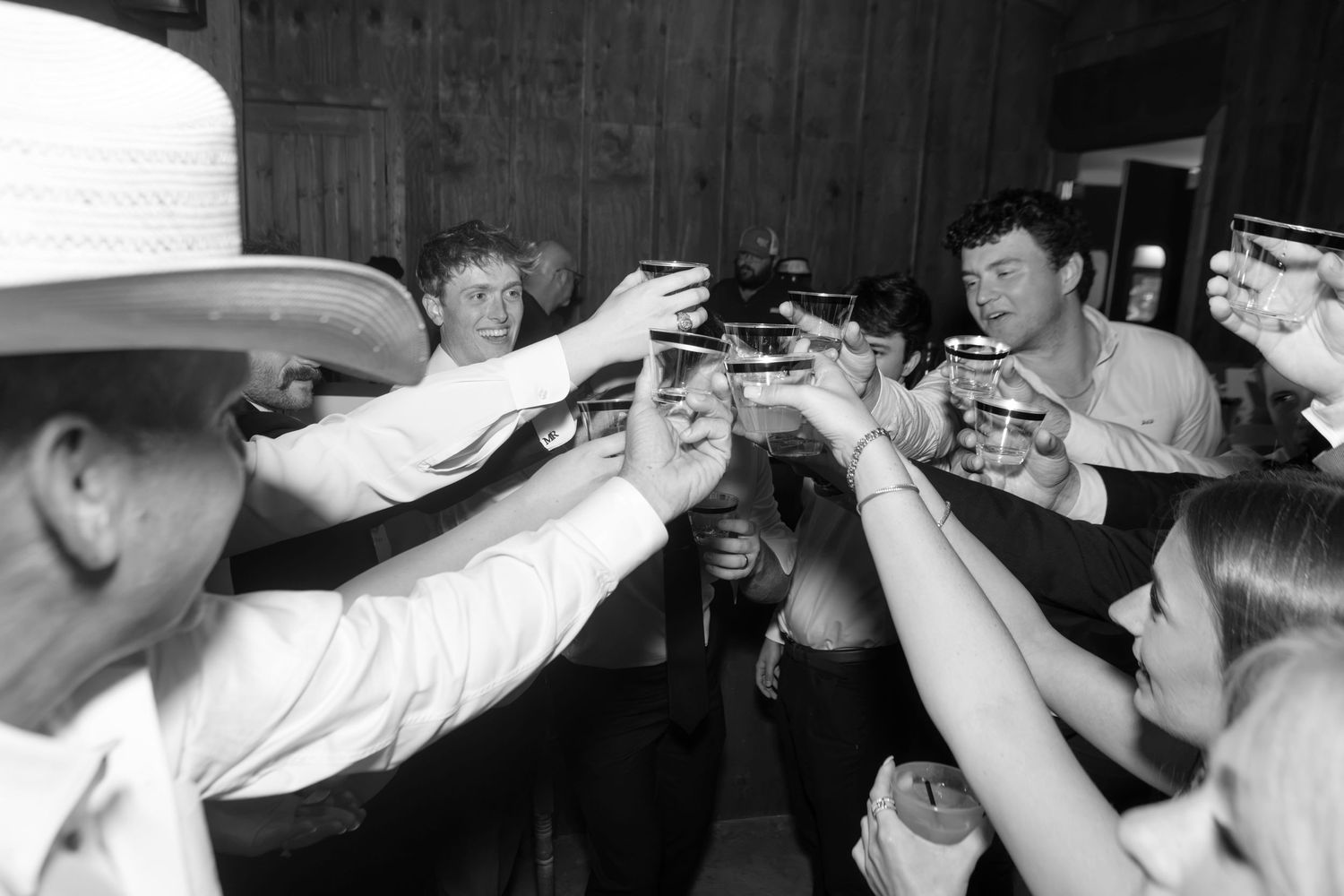 Black and white photo of a group toasting drinks together at a party, with one man wearing a cowboy hat.