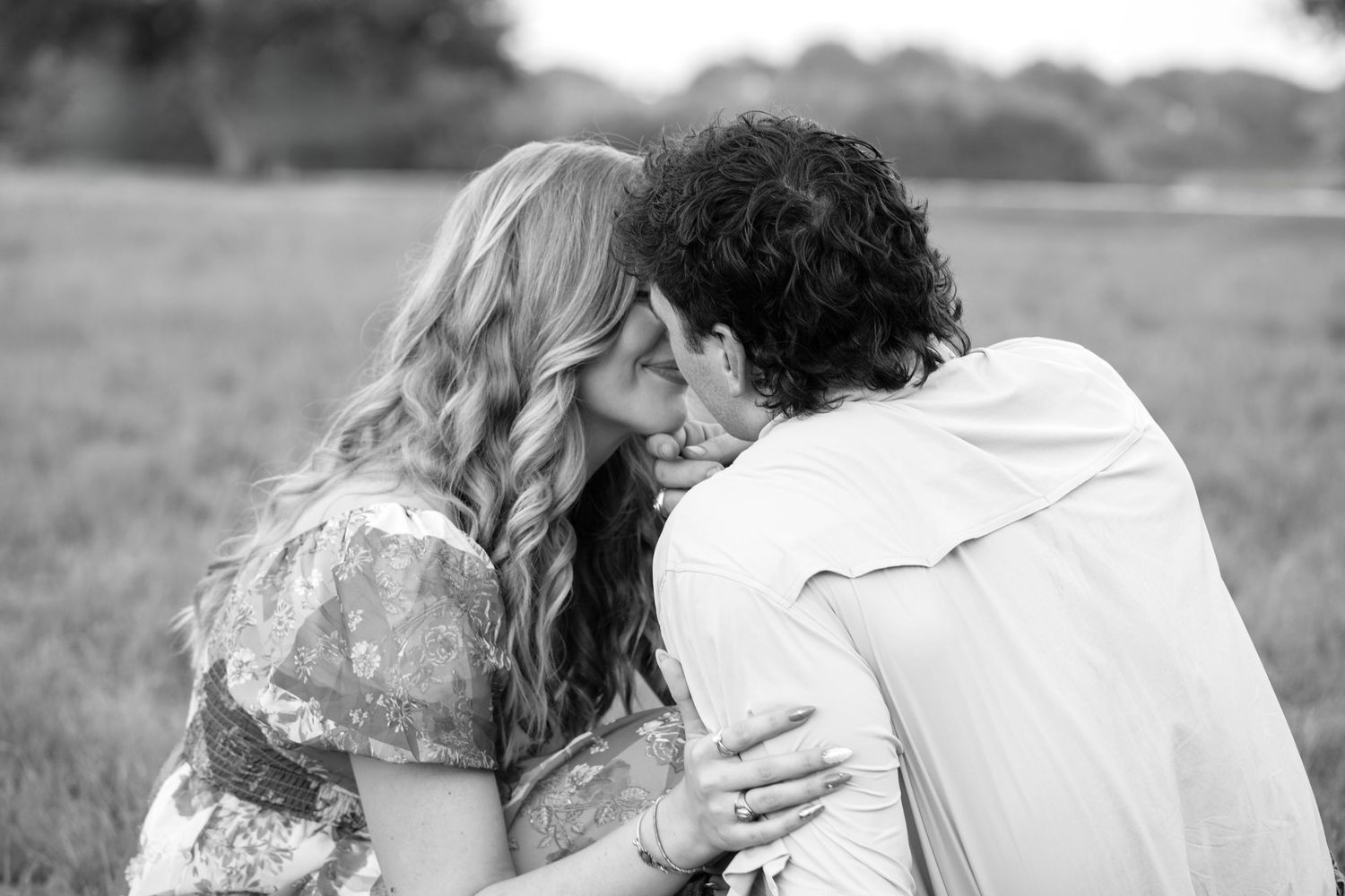 A couple shares a romantic kiss while standing in a field during a sunny day.
