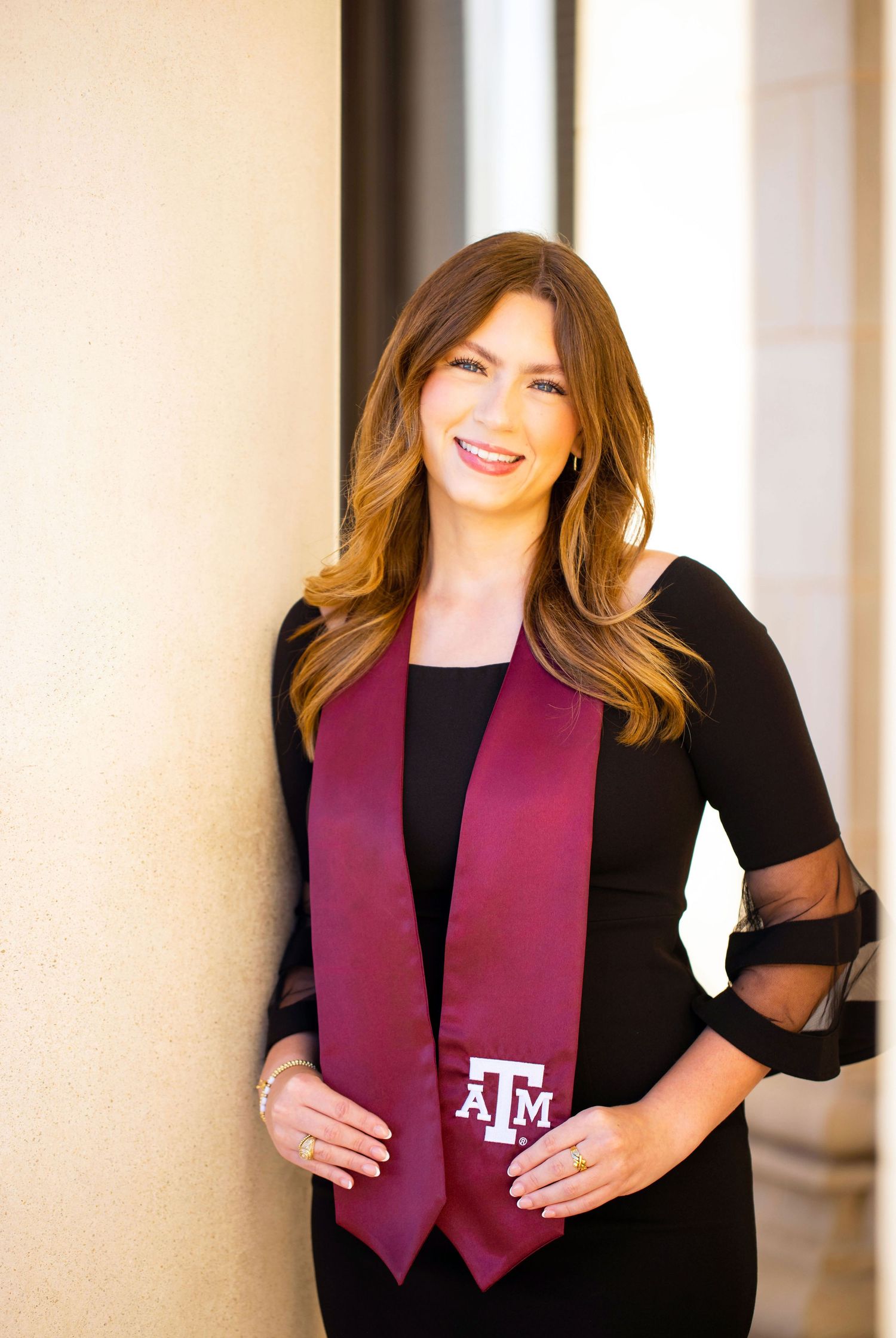 A smiling woman with long brown hair wearing a maroon scarf and black jacket.