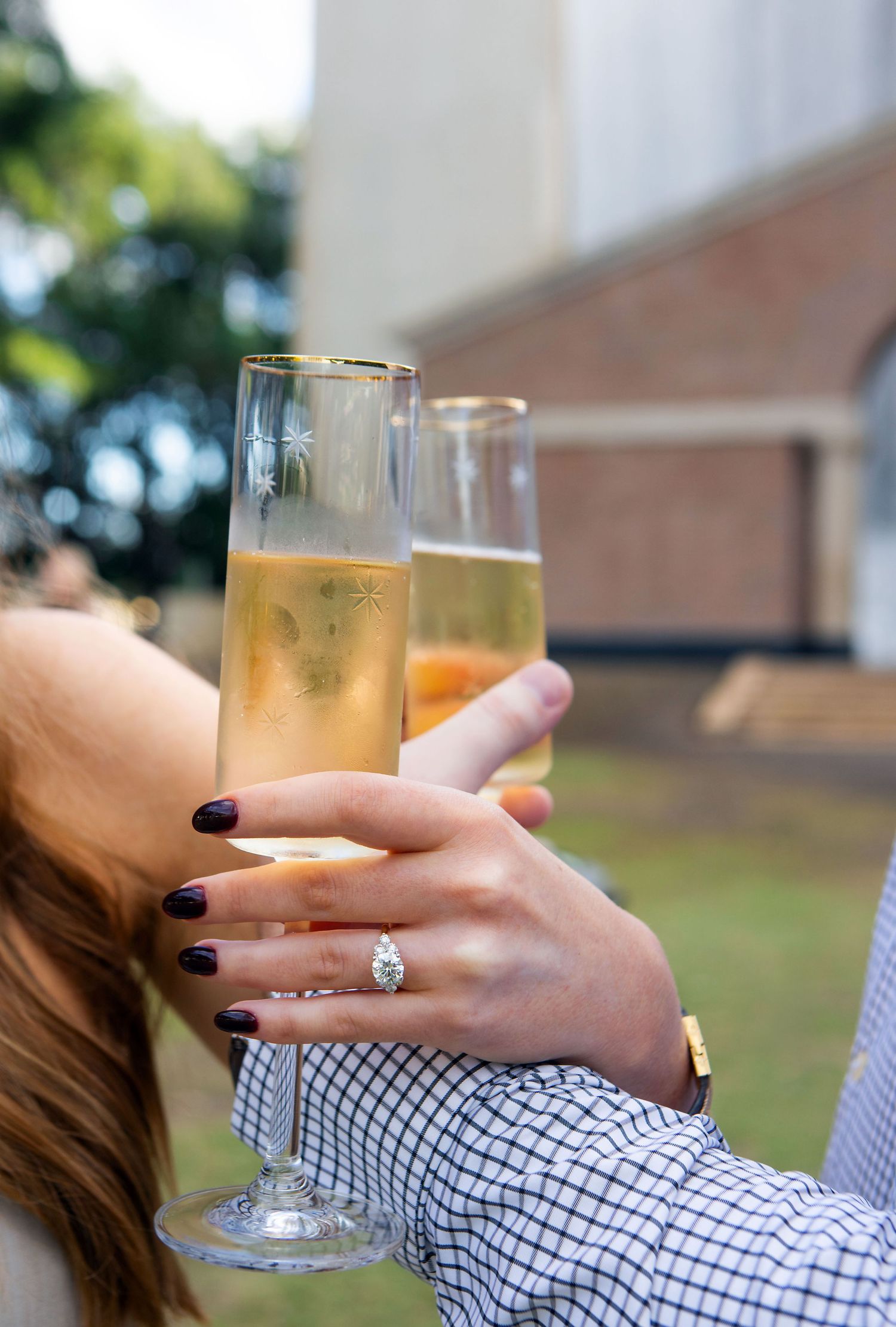 Two hands toasting with elegant gold-rimmed champagne flutes, one adorned with a diamond engagement ring.