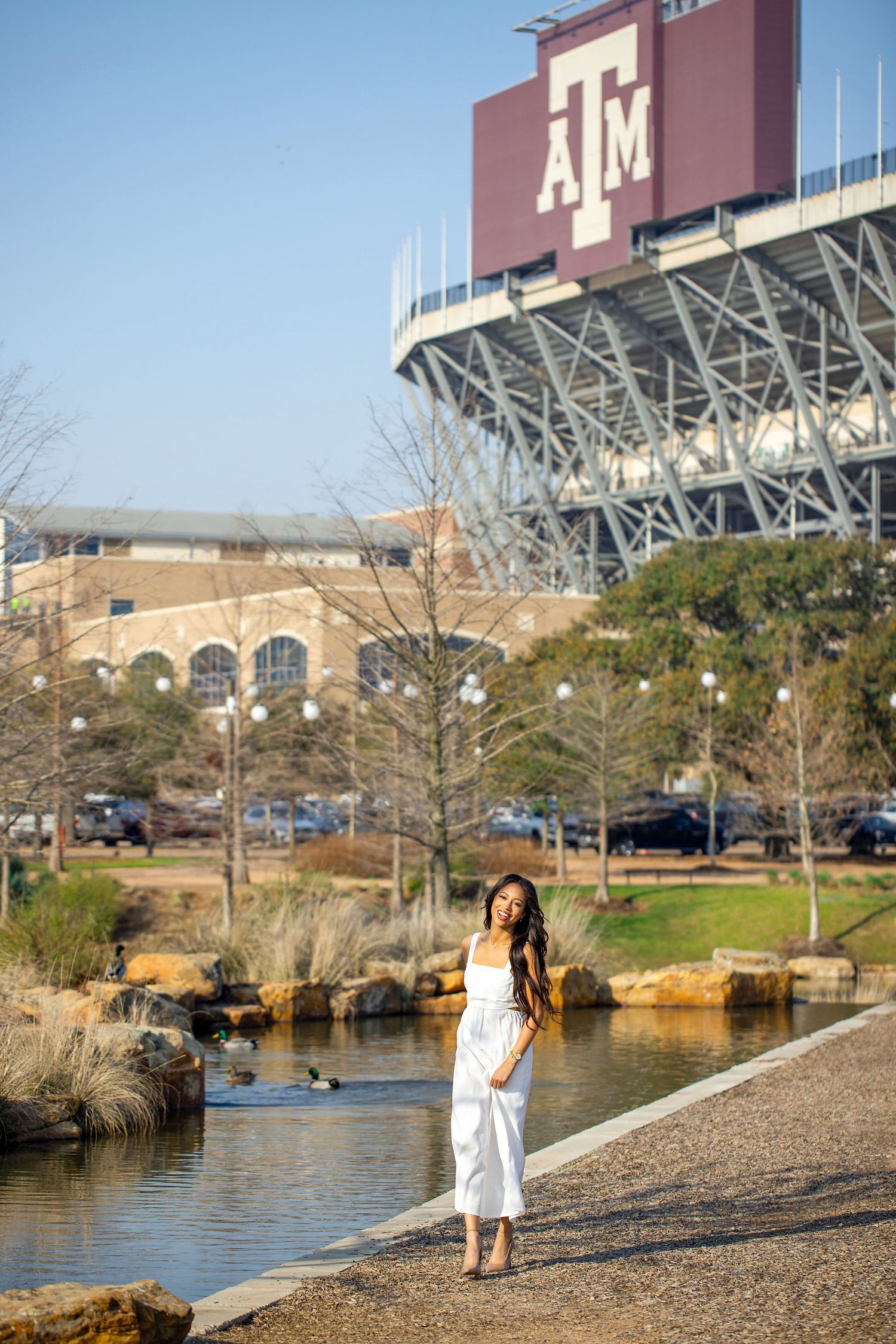 Graduation photos captured by lake with Texas A&M stadium visible in background.