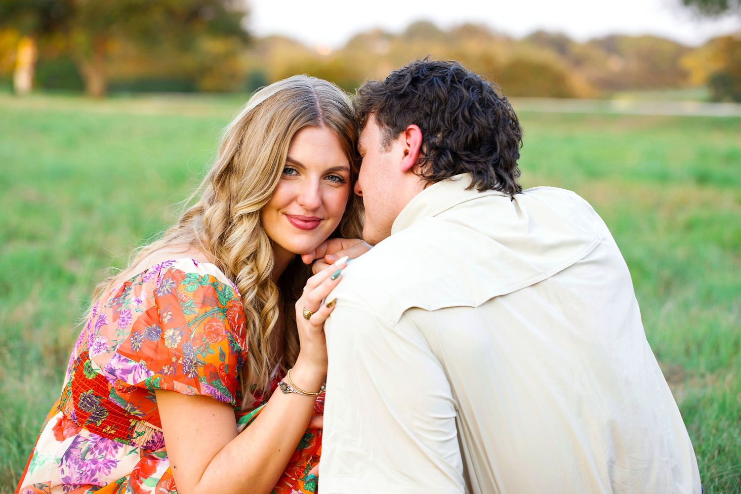 A romantic couple embraces in a sunlit meadow wearing floral and white outfits during an outdoor photo session.