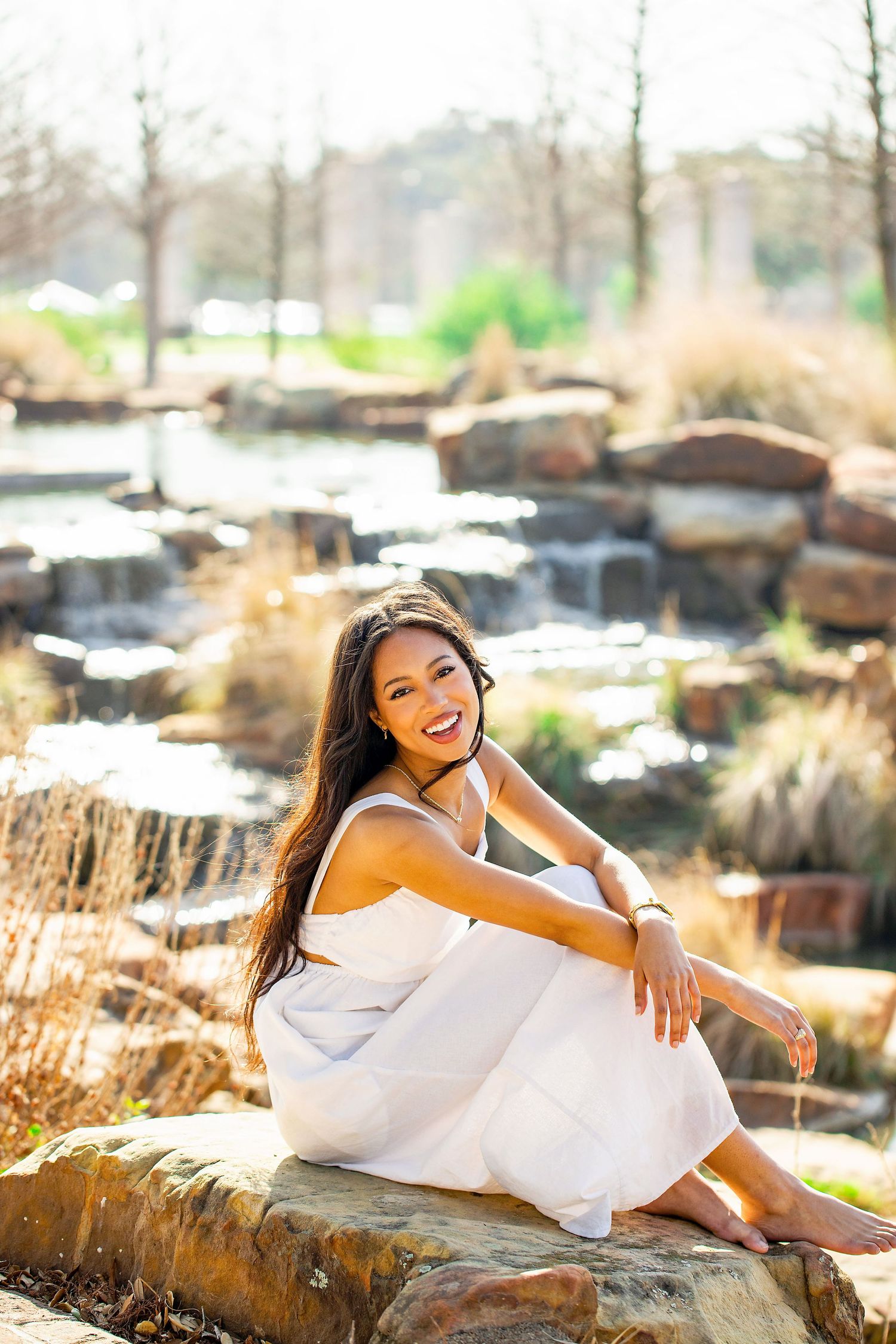 Graduate in white dress poses on rocky landscape during outdoor graduation photo session.