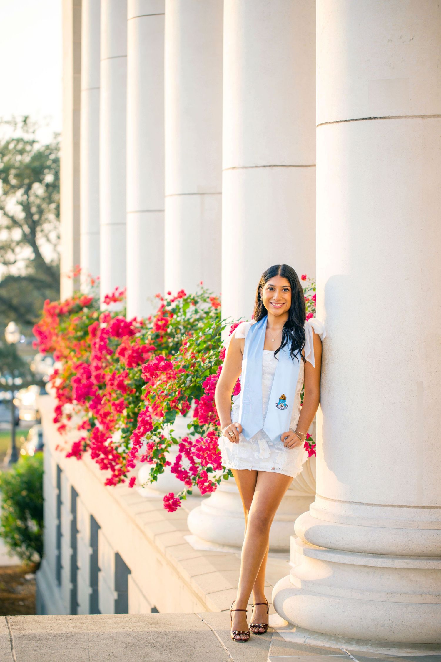 Elegant Texas A&M University graduate photoshoot white columns and vibrant pink flowers creating a classic architectural backdrop.