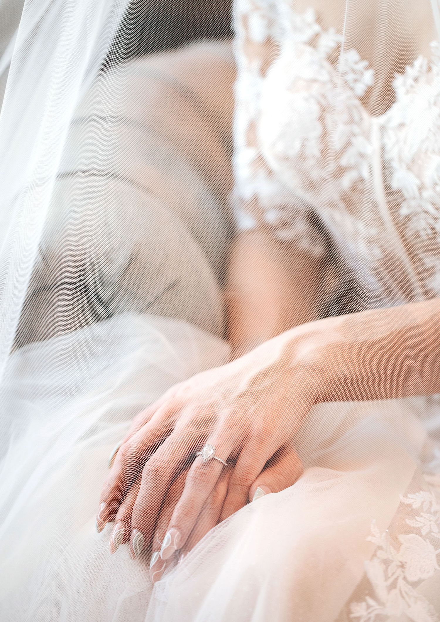 Close-up view of hands wearing engagement rings resting on delicate white lace fabric.